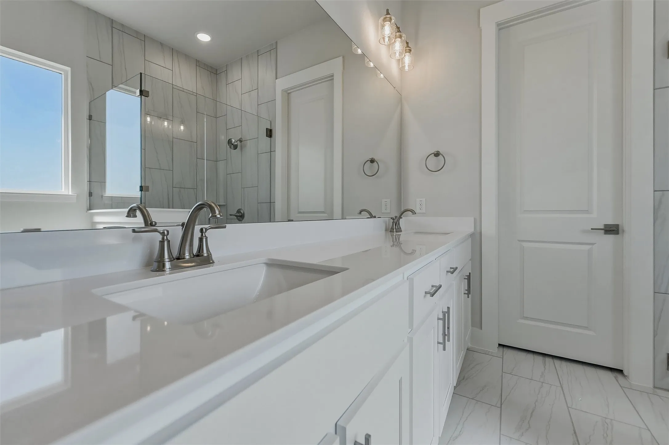 Dual vanity with white cabinetry, integrated sinks, brushed nickel fixtures, and a glass-enclosed shower with tile surround
