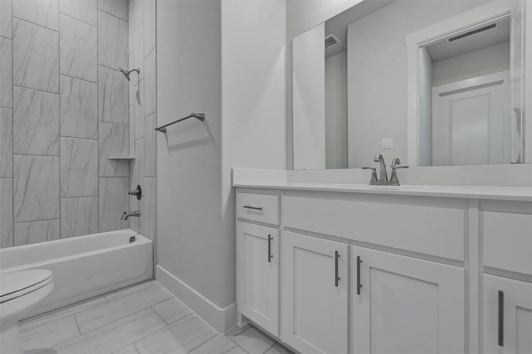 White vanity with integrated sink, brushed nickel faucet, large vanity mirror, full-height tiled shower surround, and a built-in shower shelf