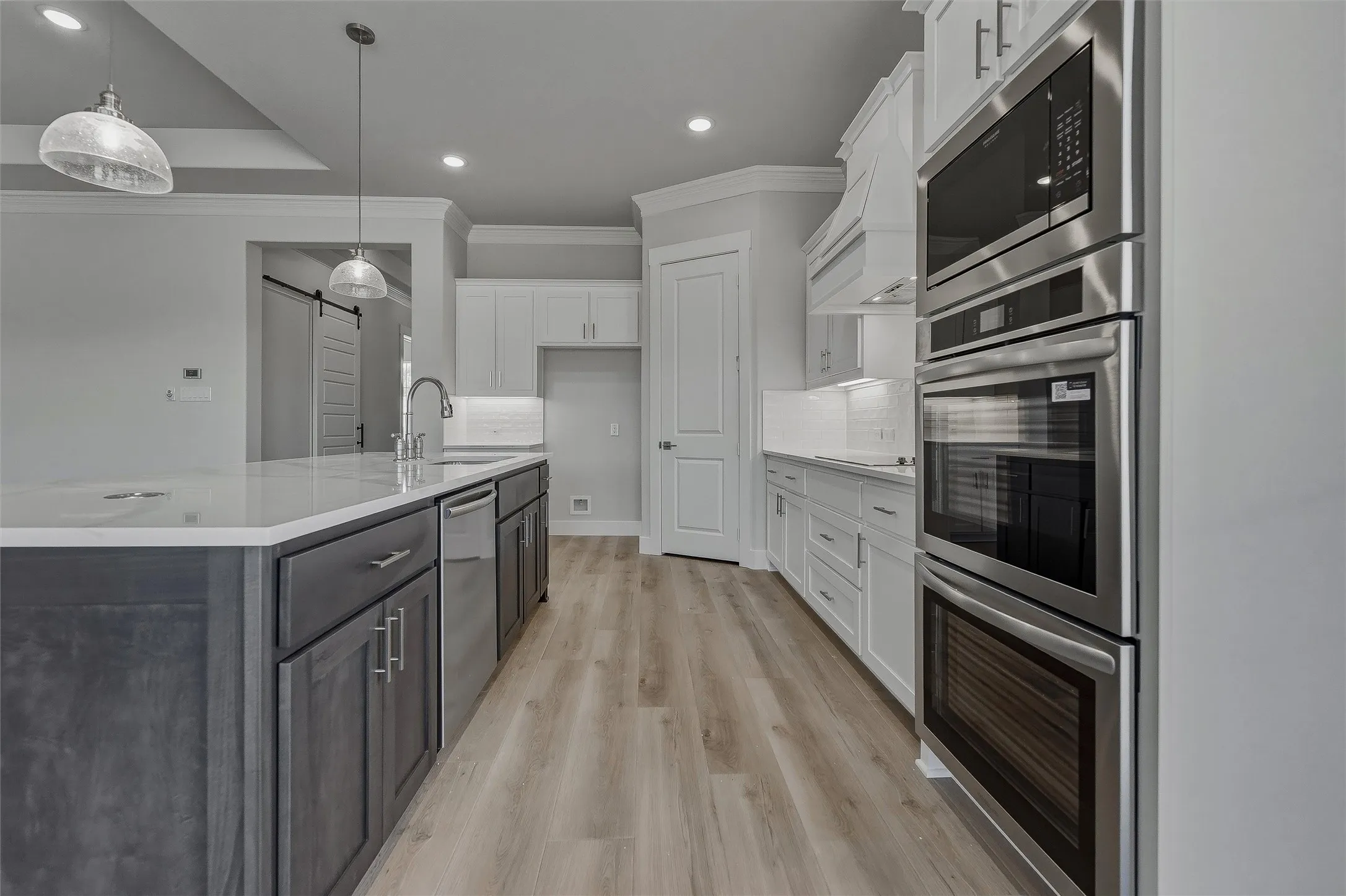 Modern kitchen featuring stainless steel built-in appliances, a large island with sink, white shaker cabinetry, and wood-finish flooring