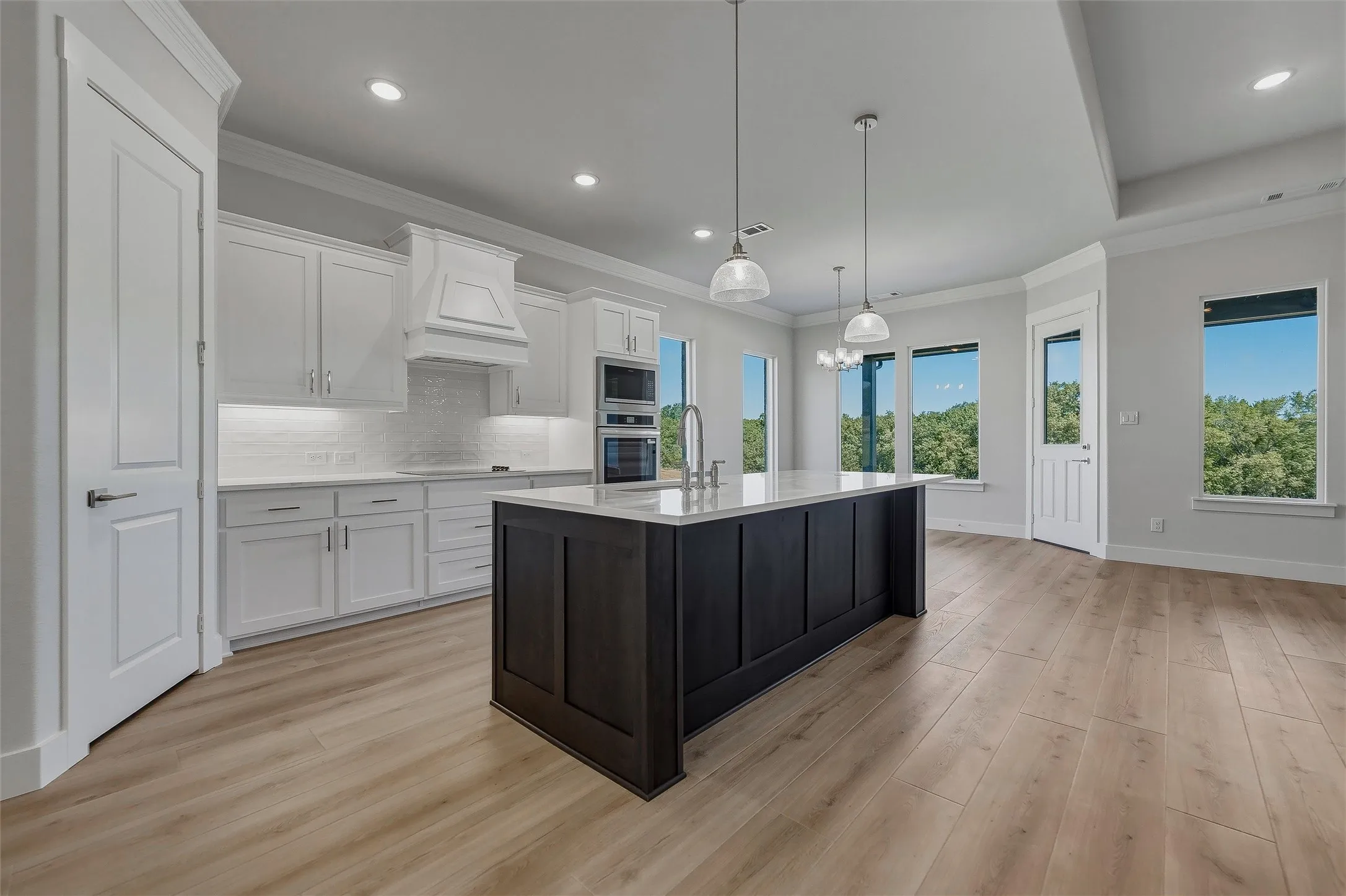 Open-concept kitchen with a large dark-tone island, white cabinetry, integrated stainless steel appliances, and wood-finish flooring