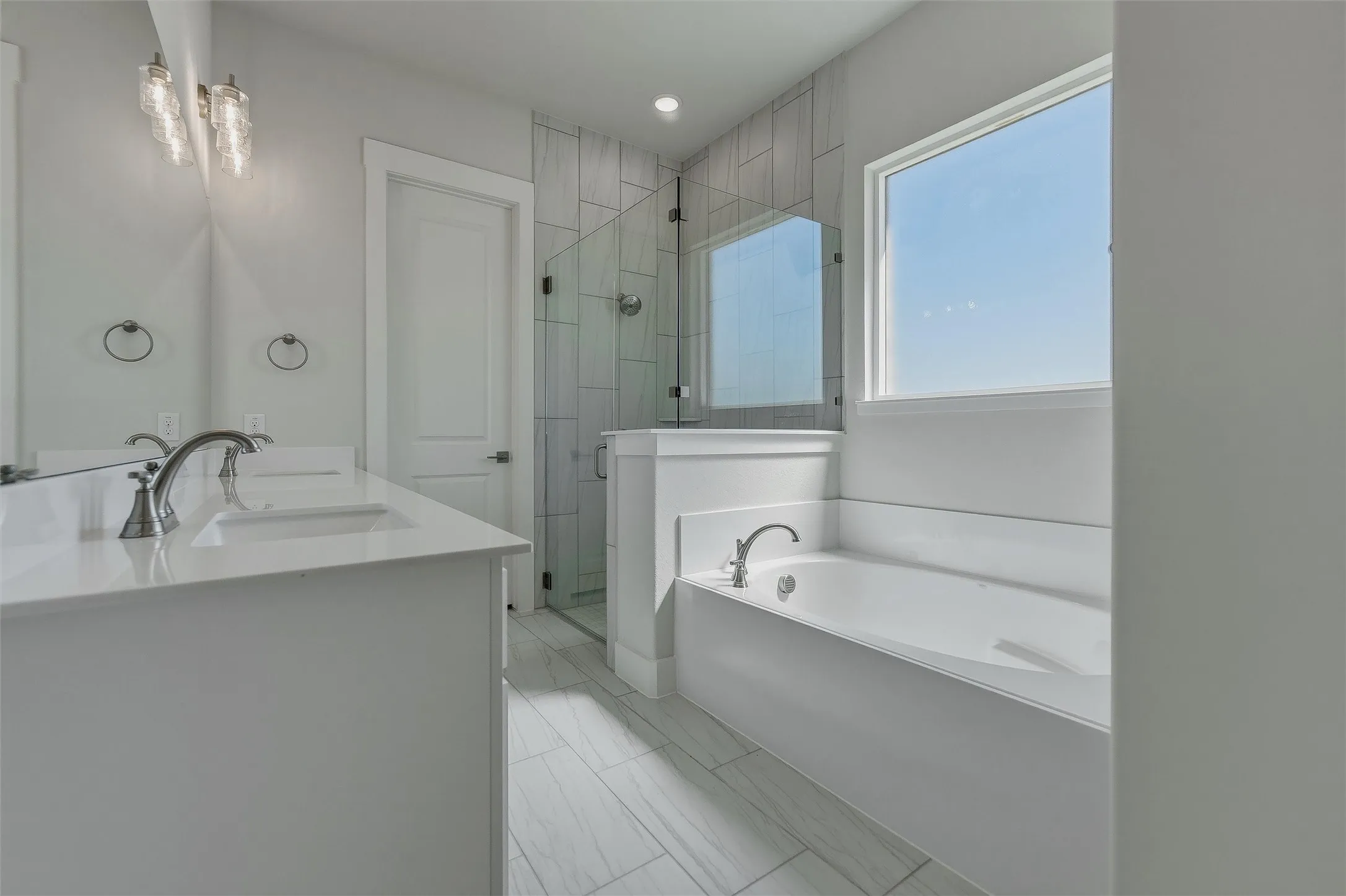 Dual vanity with integrated sinks, a built-in soaking tub, a walk-in shower with glass enclosure, and wood-finish tile flooring