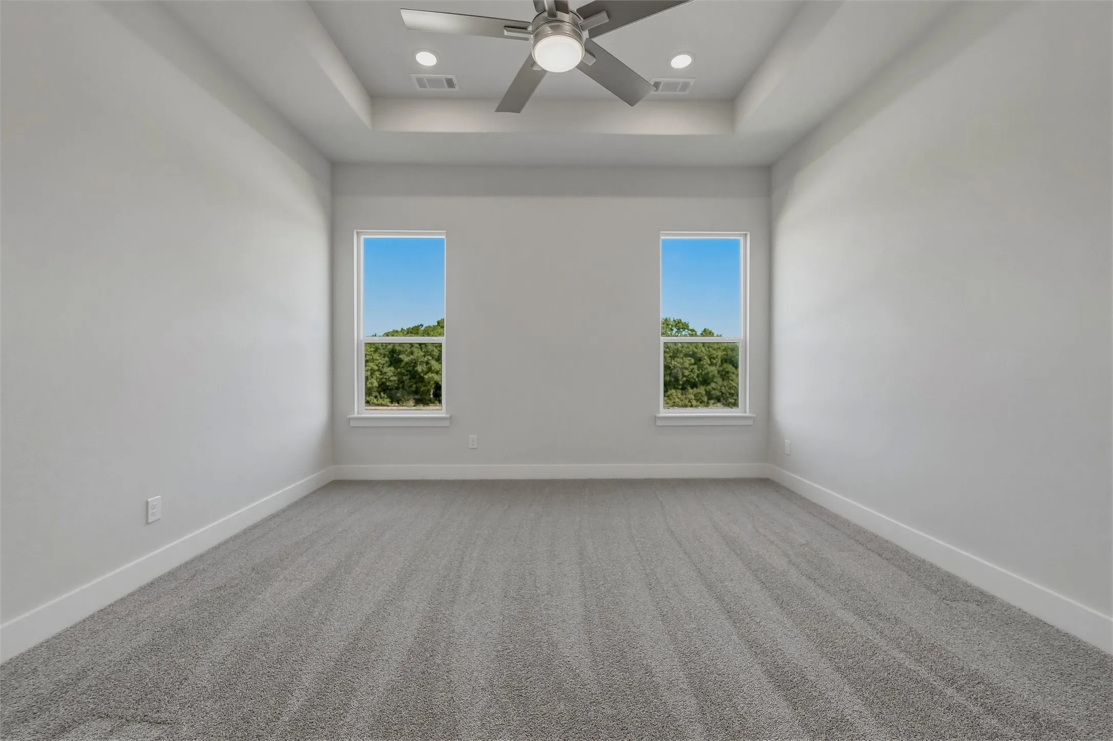 Recessed lighting, ceiling fan, tray ceiling, two windows, and gray carpet