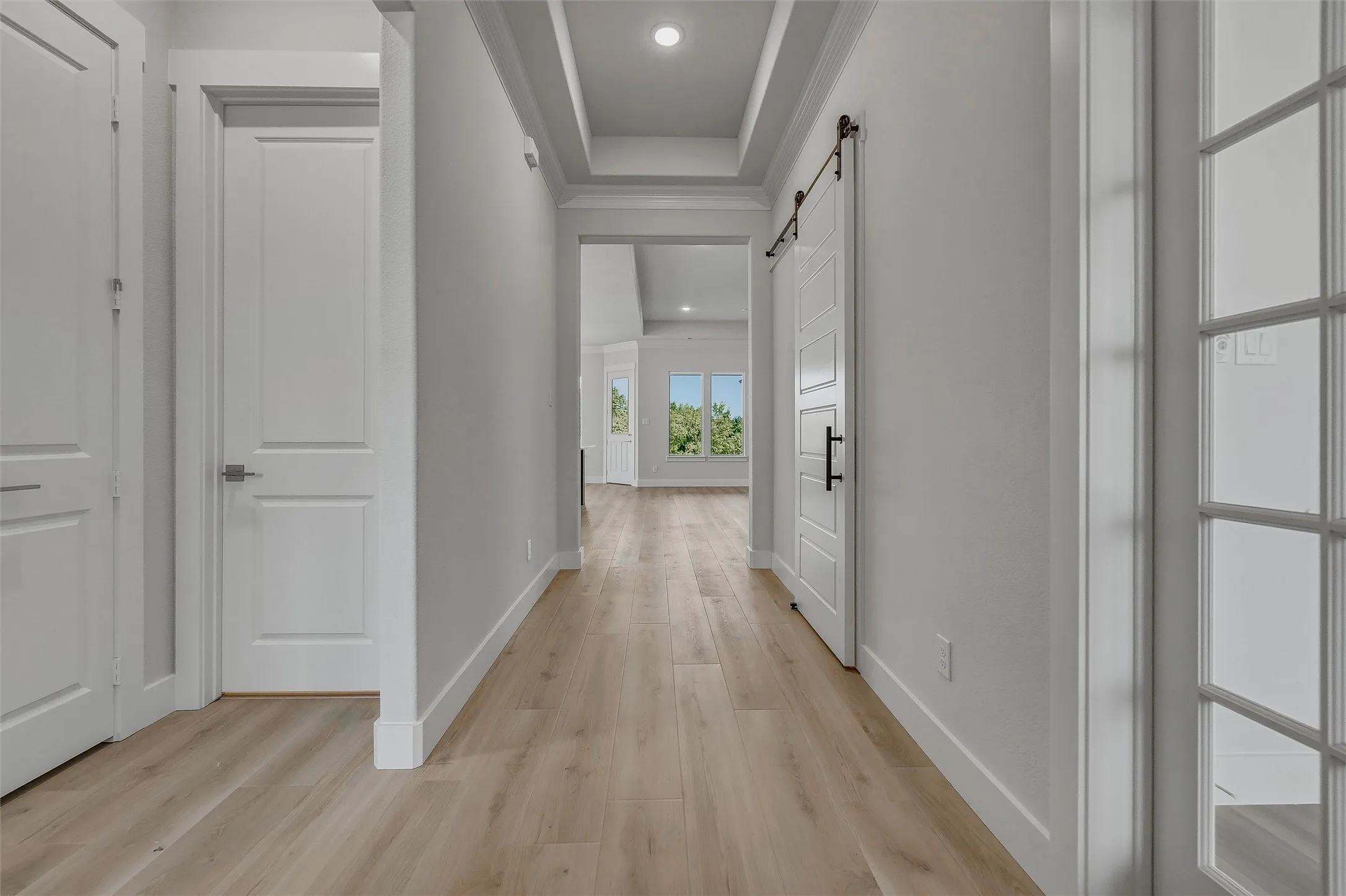 Wood-finish flooring, recessed lighting, white trim, white interior doors, and a white barn door with black hardware
