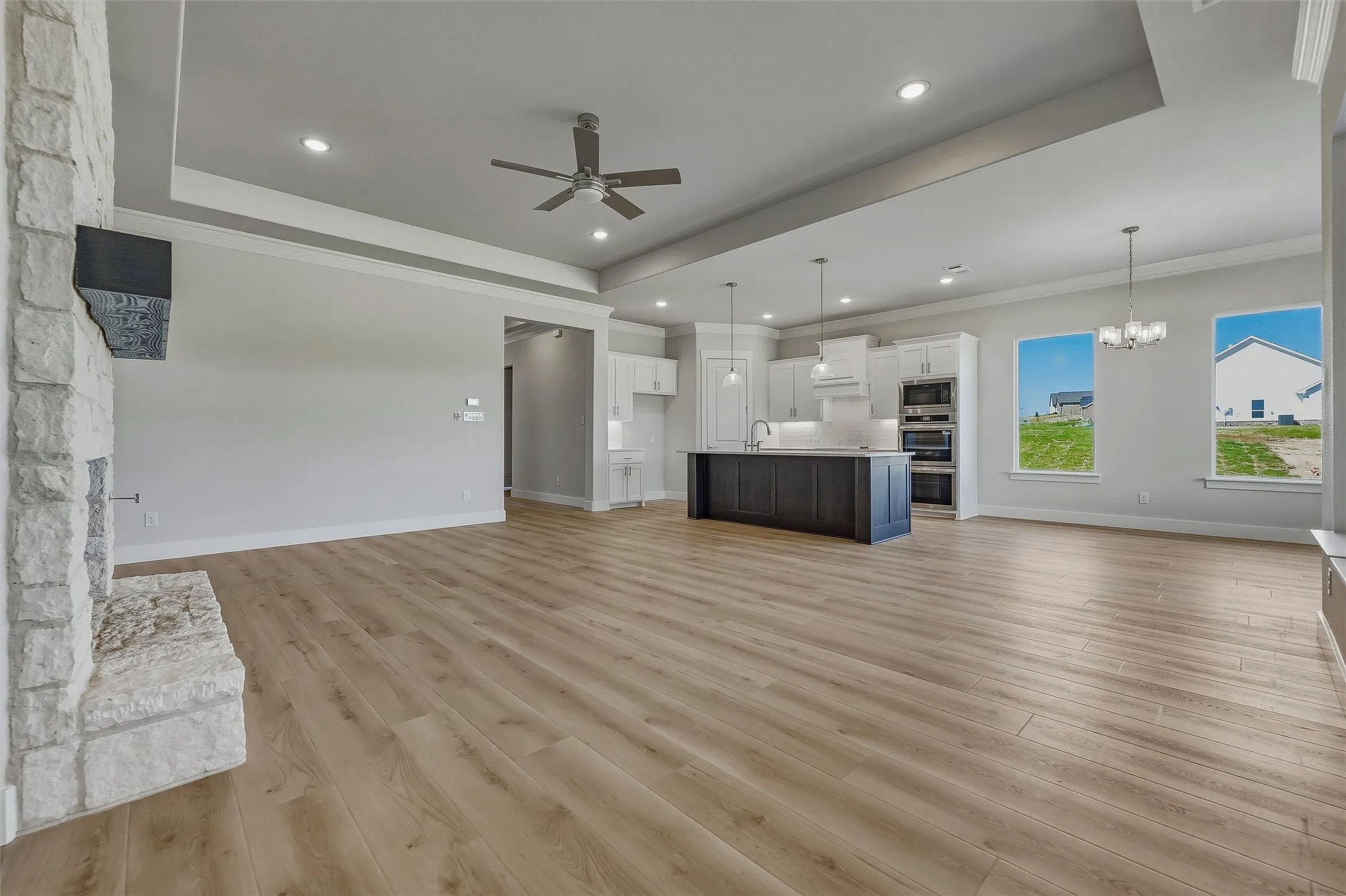 Open-concept living area featuring wood-finish flooring, a stone fireplace, recessed lighting, and a tray ceiling with a ceiling fan