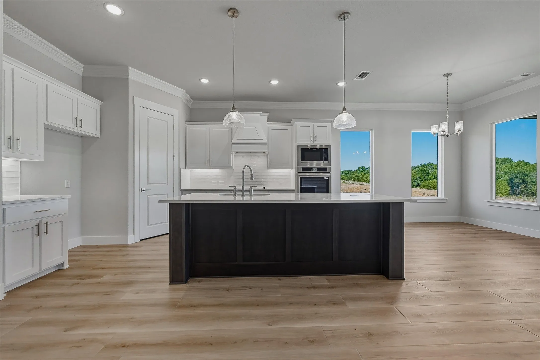 Kitchen featuring a dark-toned island with a stainless steel sink, light-toned cabinetry, light wood-finish flooring, and integrated stainless steel appliances
