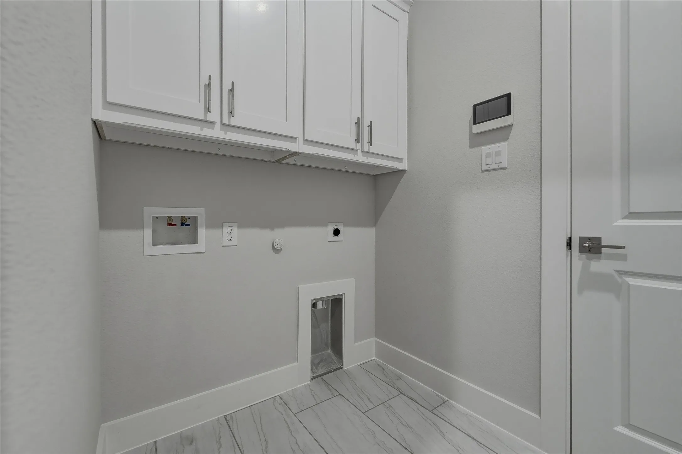 White shaker-style cabinetry with silver hardware, light gray walls, white trim, and wood-finish tile flooring