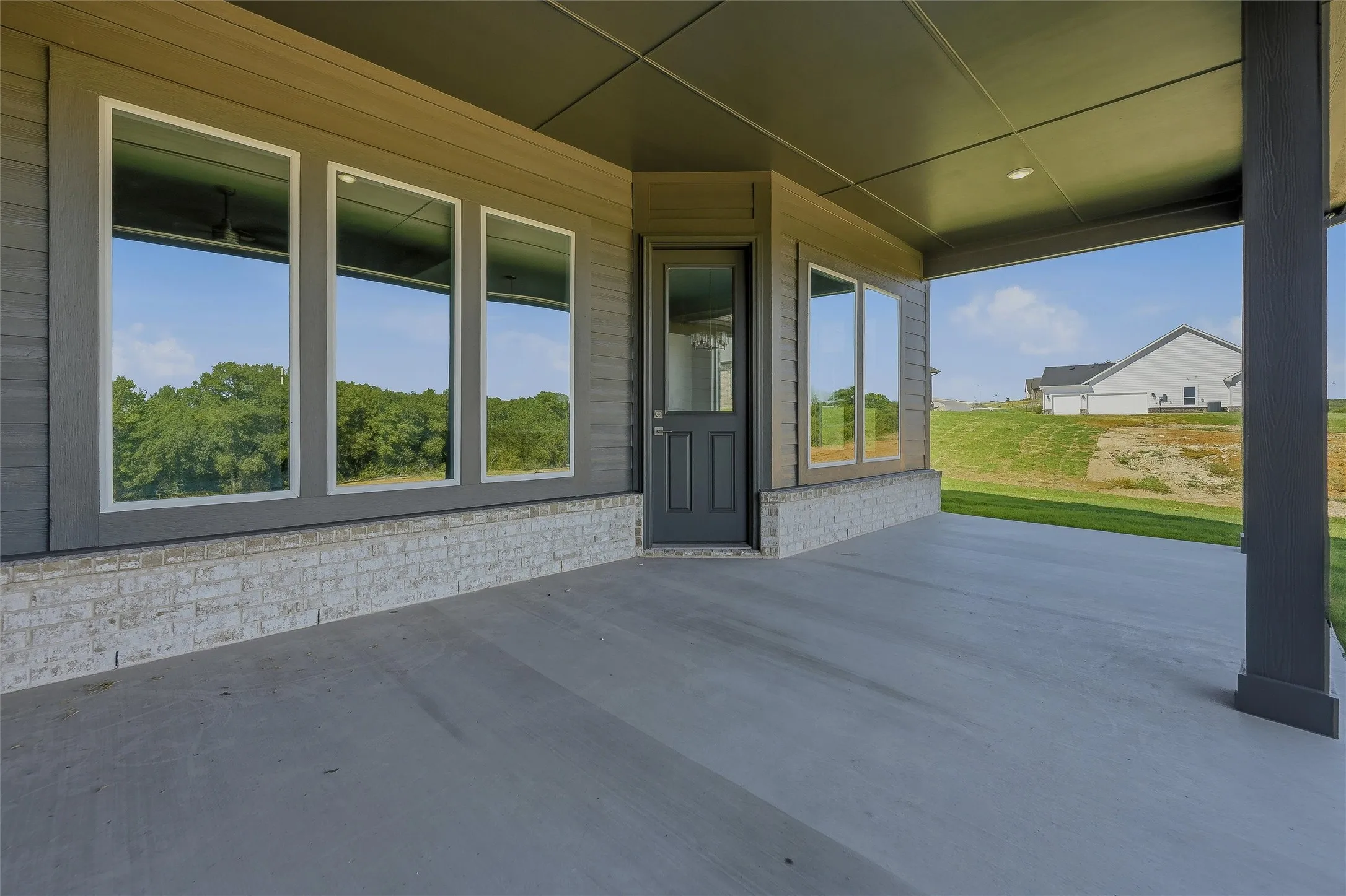 Covered patio with a concrete surface, white brick accents, and large windows