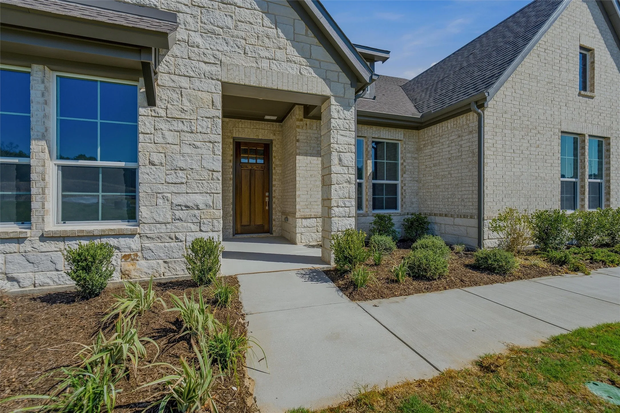 Stone facade with a covered entry, dark wood-finish front door, and established landscaping