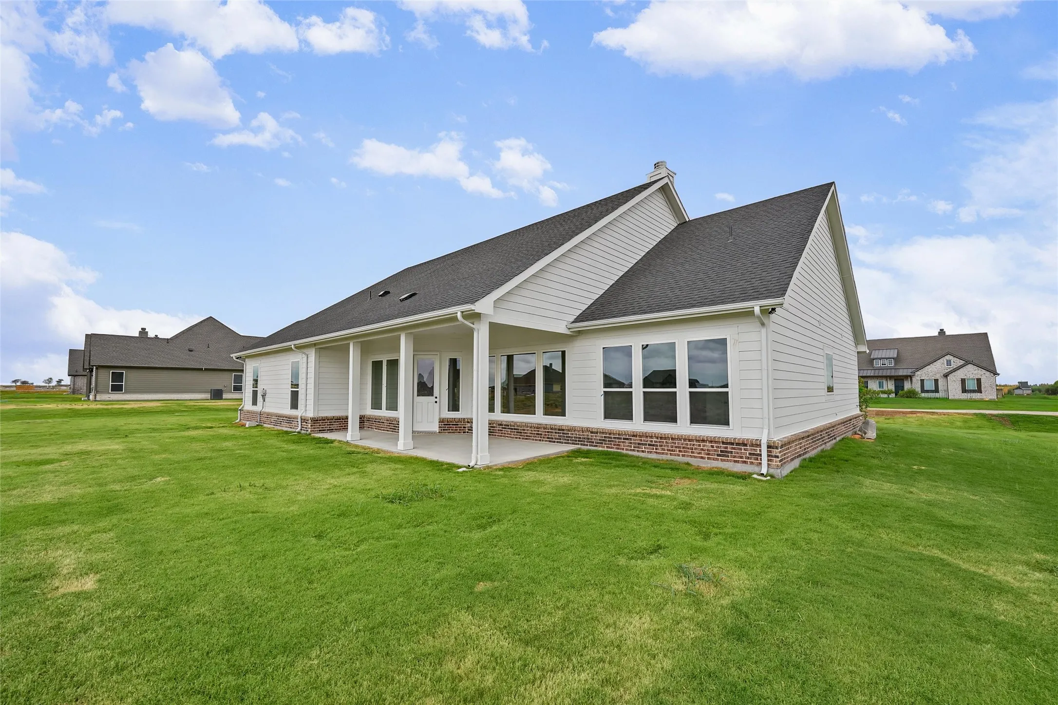 Expansive rear lawn, covered patio, white siding exterior, brick foundation, and dark shingle roof