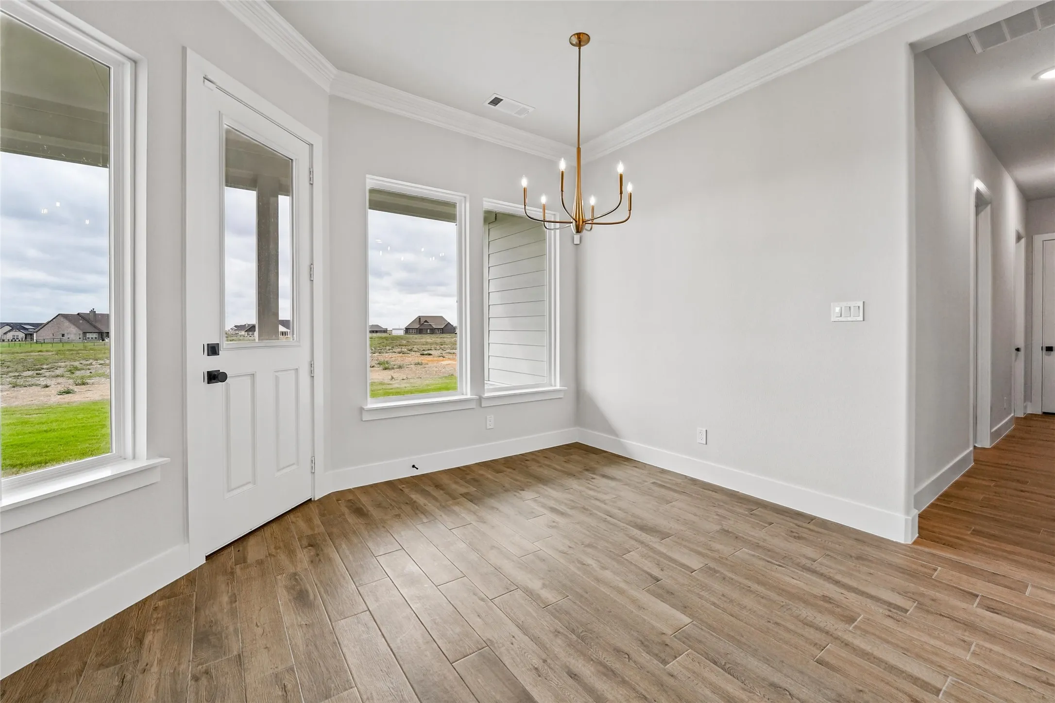 Wood-finish tile flooring, white walls, and a multi-light brass chandelier