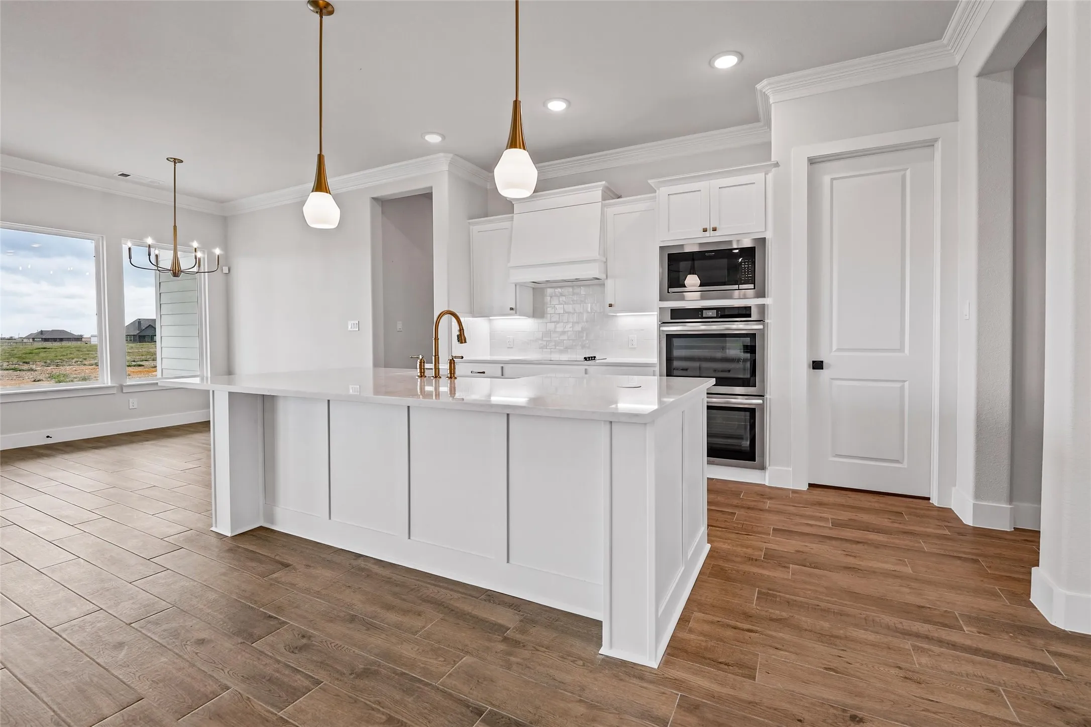 Gourmet kitchen featuring a large island with pendant lighting, stainless steel double ovens, and wood-finish flooring
