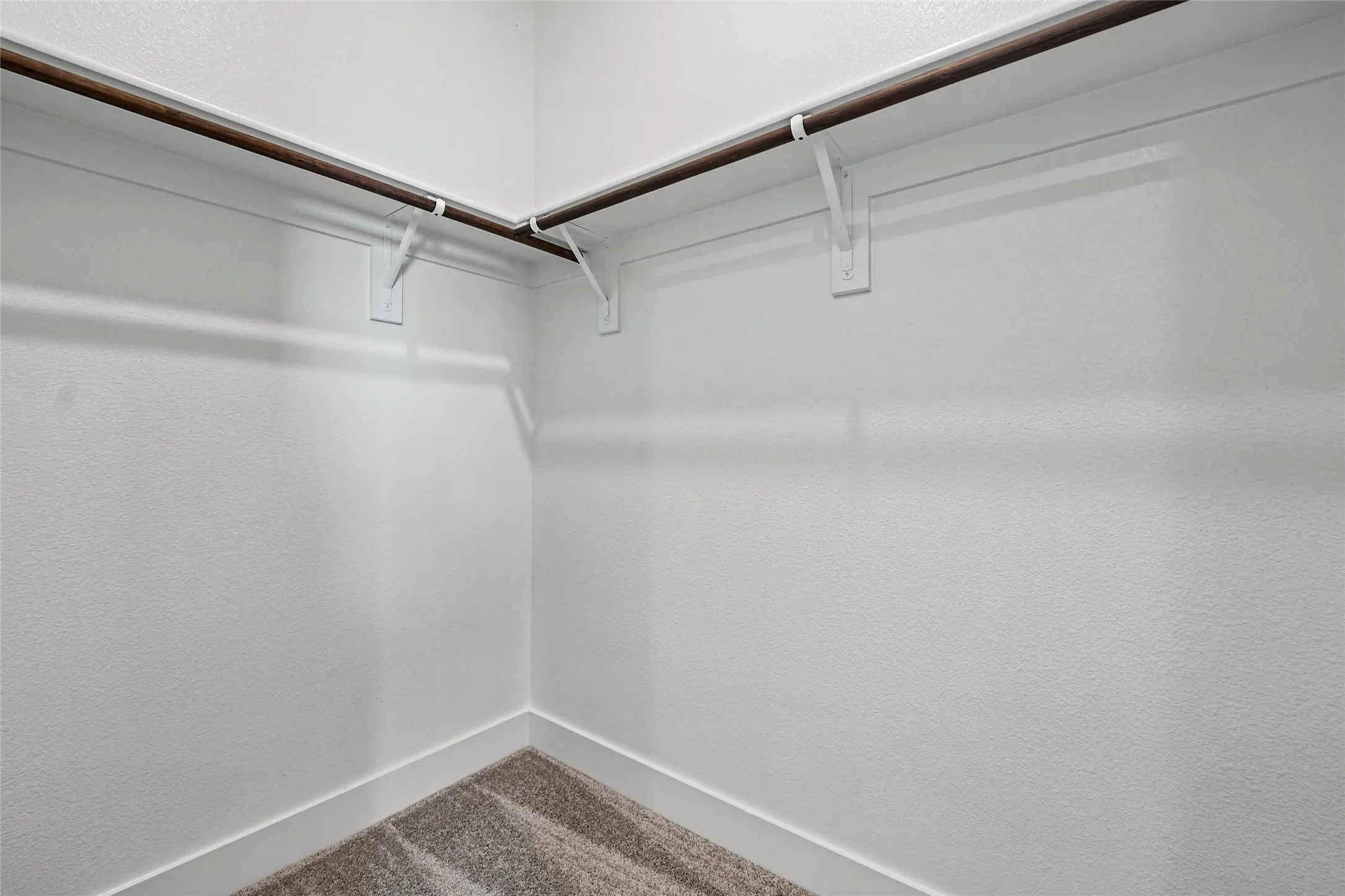 Carpeted closet with a wood-finish hanging rod and white wall brackets