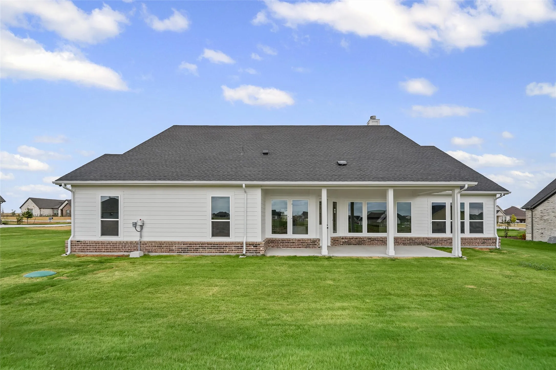 Expansive green lawn, covered patio, brick and siding exterior, multiple windows, and a dark shingle roof