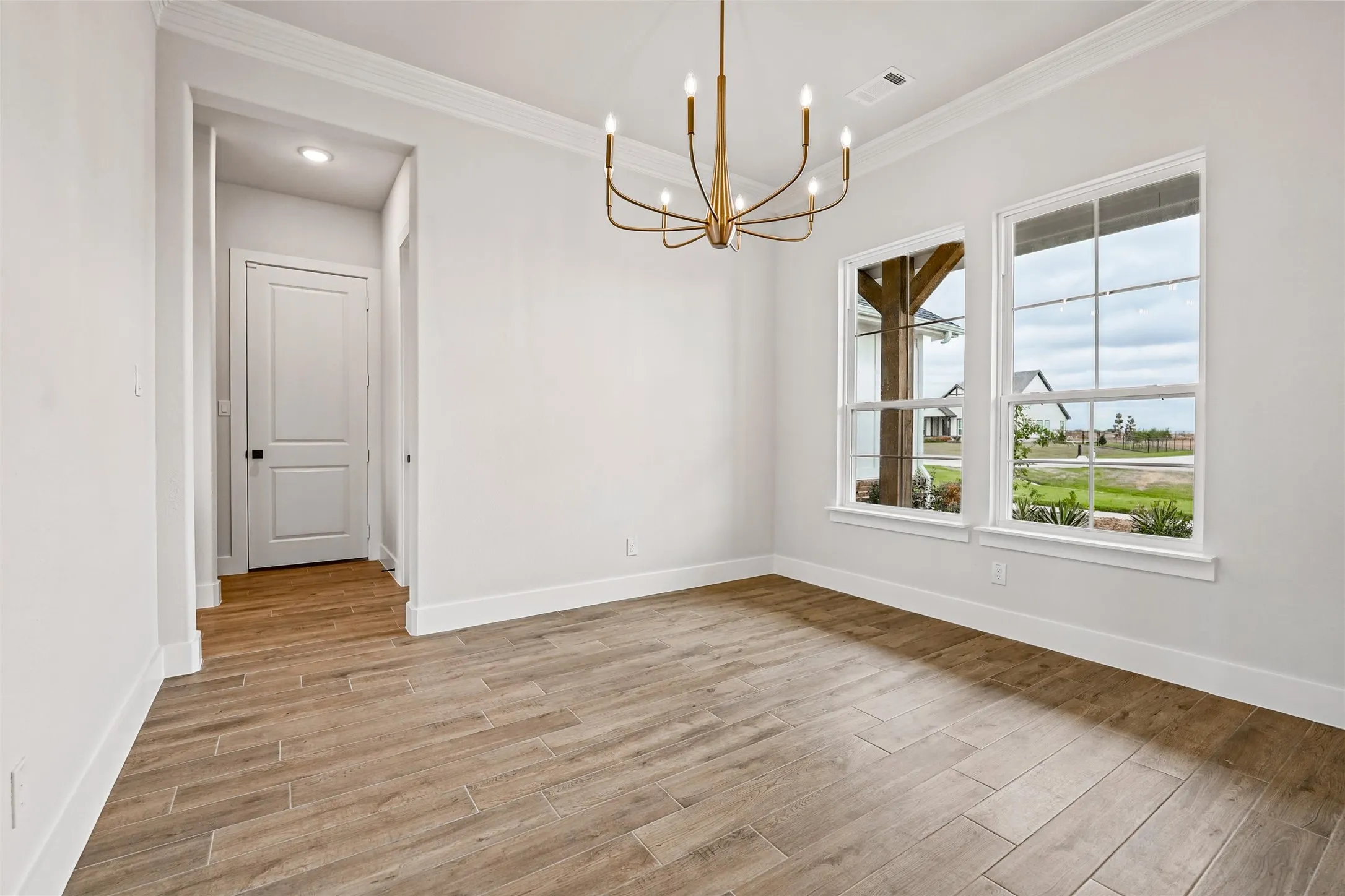 Wood-look tile flooring, crown molding, and a bronze-finish chandelier