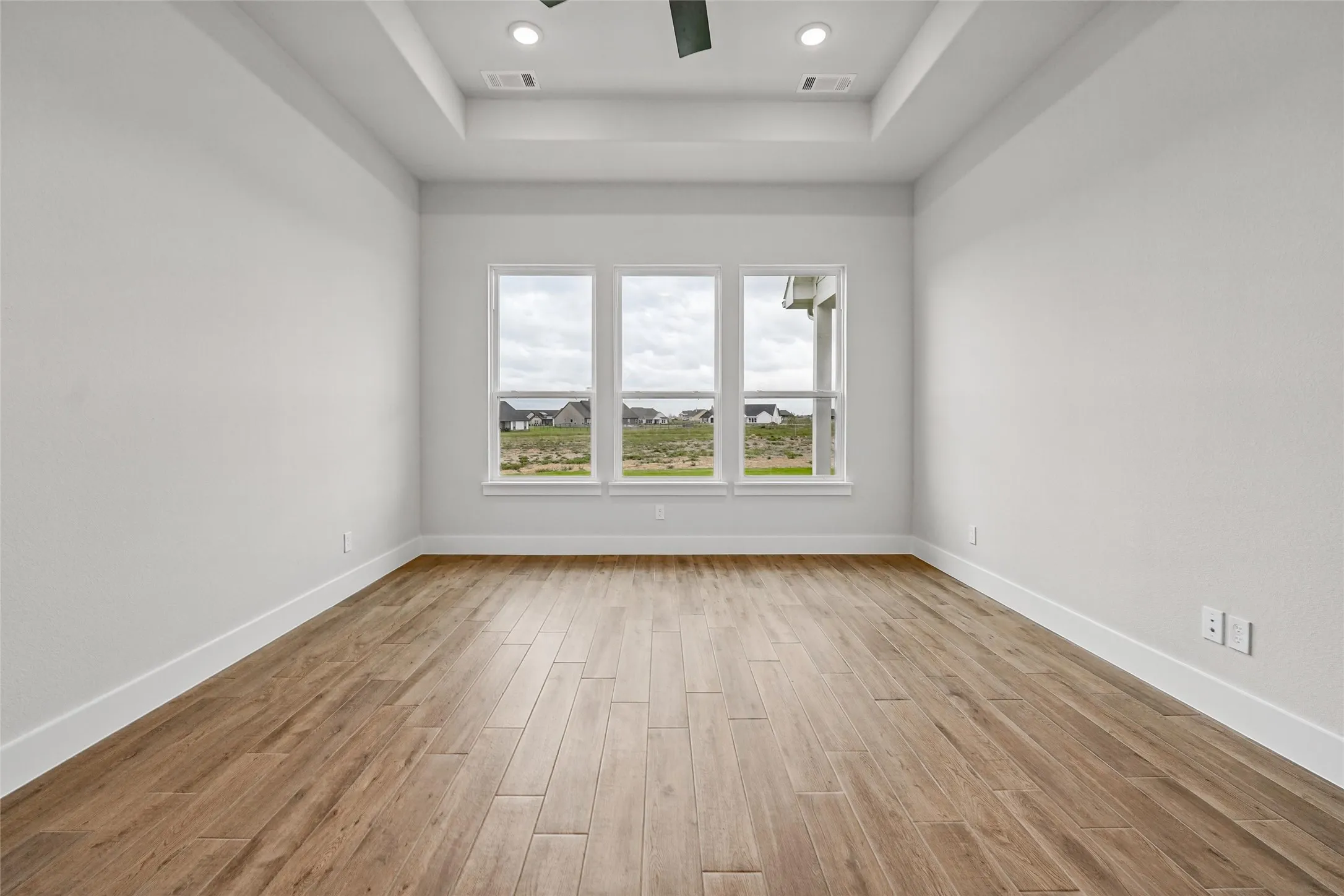 Tray ceiling with recessed lighting, wood-finish flooring, and multiple windows