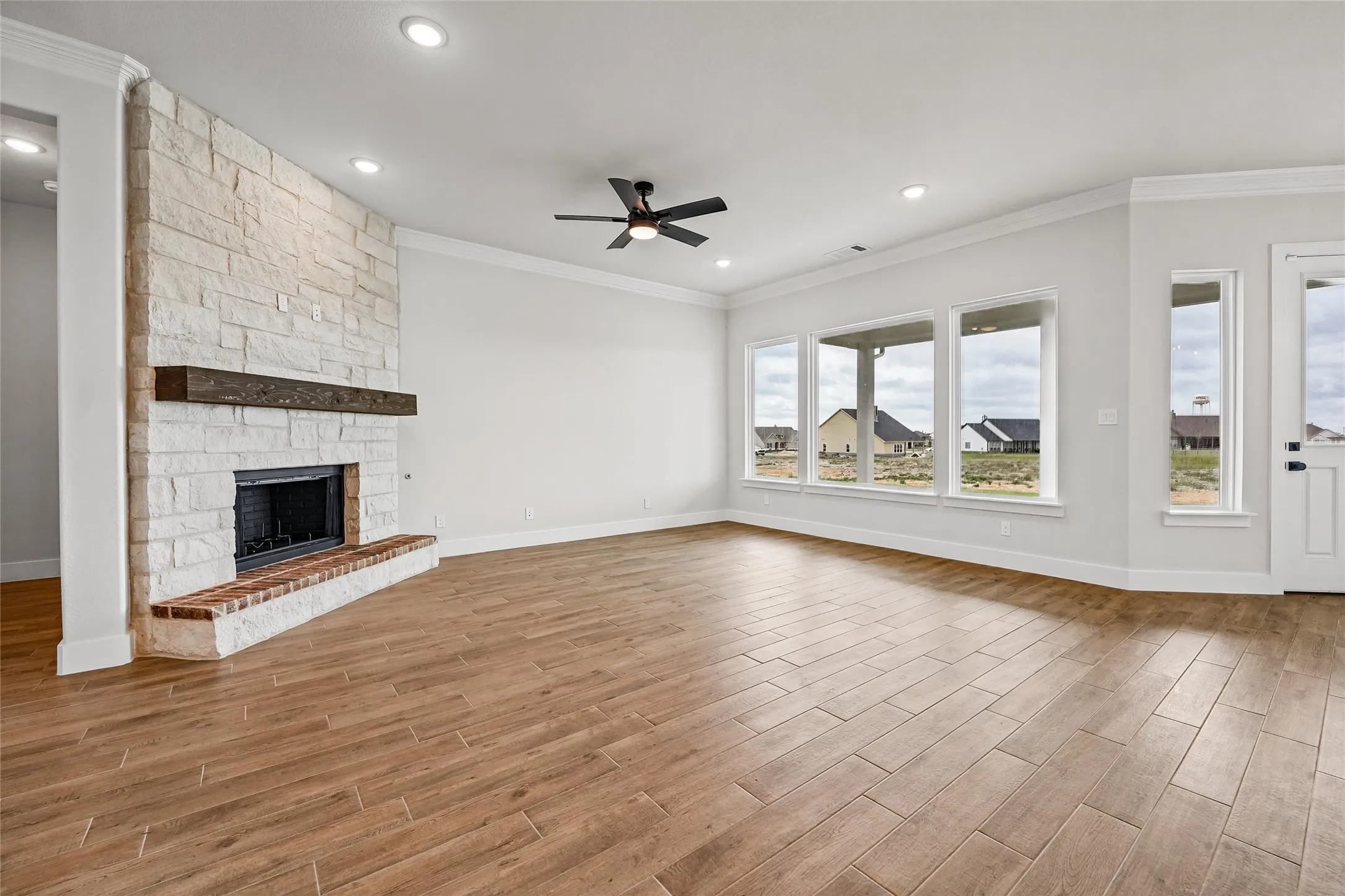 Spacious room featuring wood-finish tile flooring, a stone fireplace with a substantial wood mantel, a ceiling fan, and recessed lighting