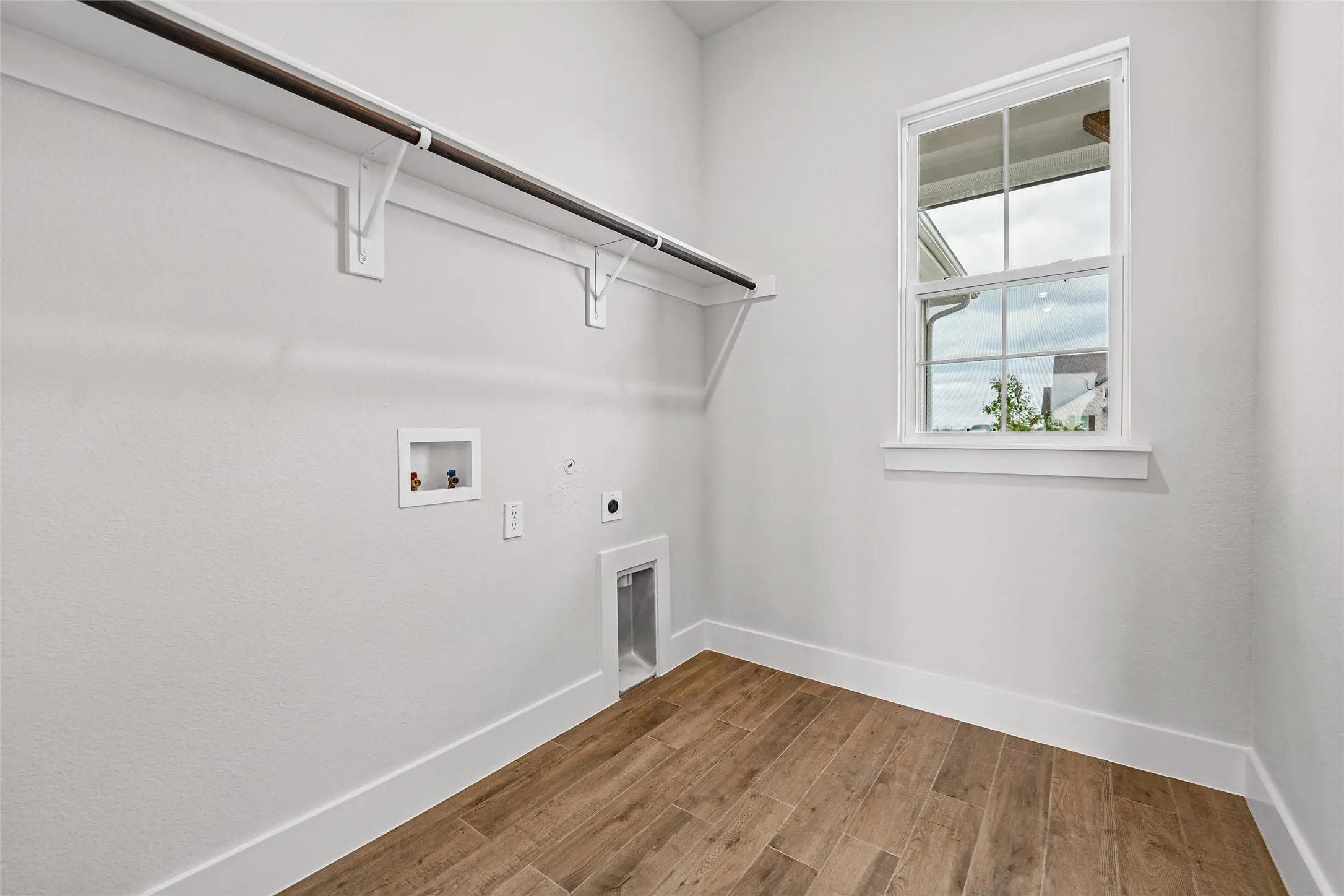 Laundry area with wood-finish flooring, a single window, and a clothes hanging rod