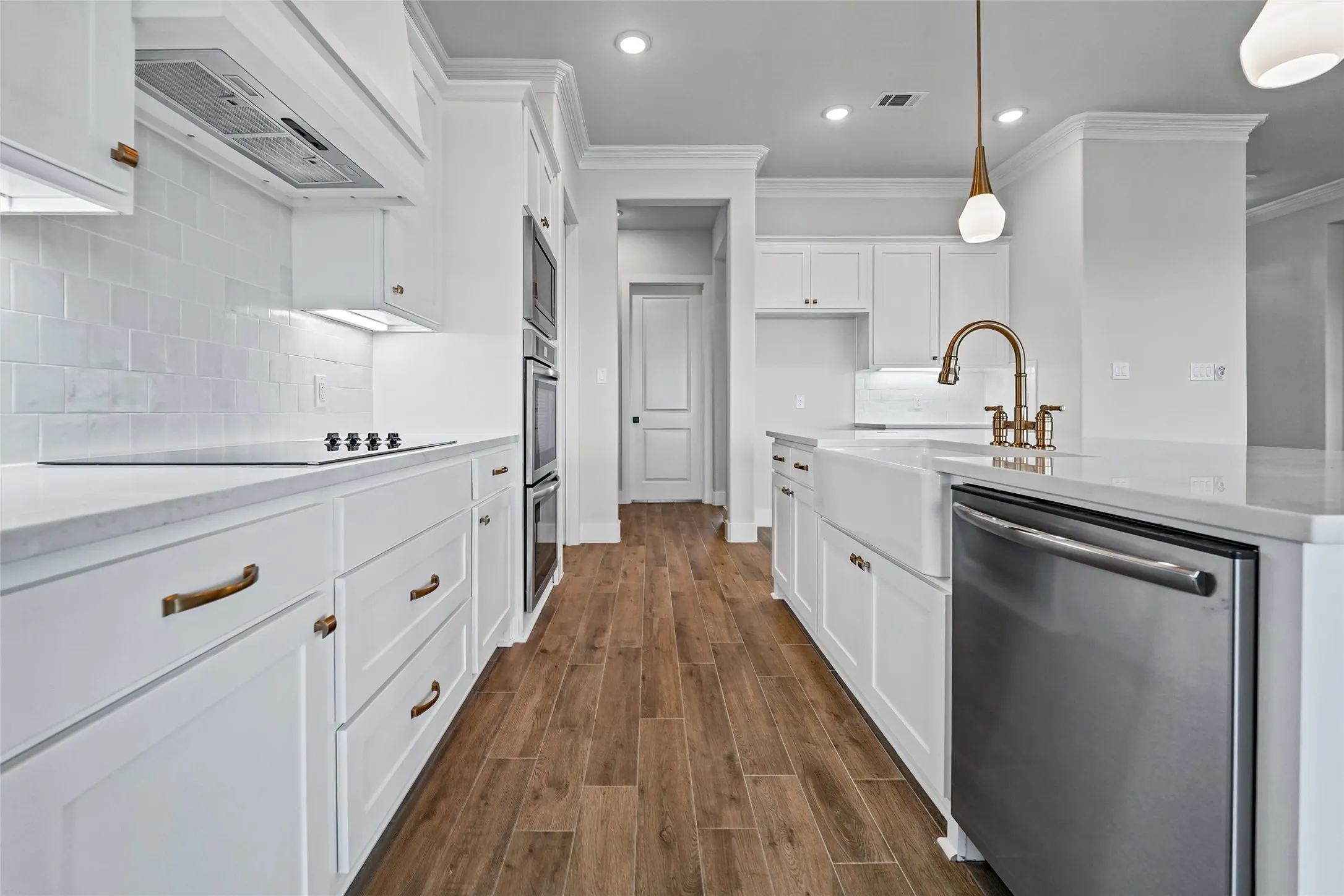 Gourmet kitchen featuring wood-finish flooring, white cabinetry with bronze hardware, stainless steel appliances, a farmhouse sink, and white subway tile backsplash