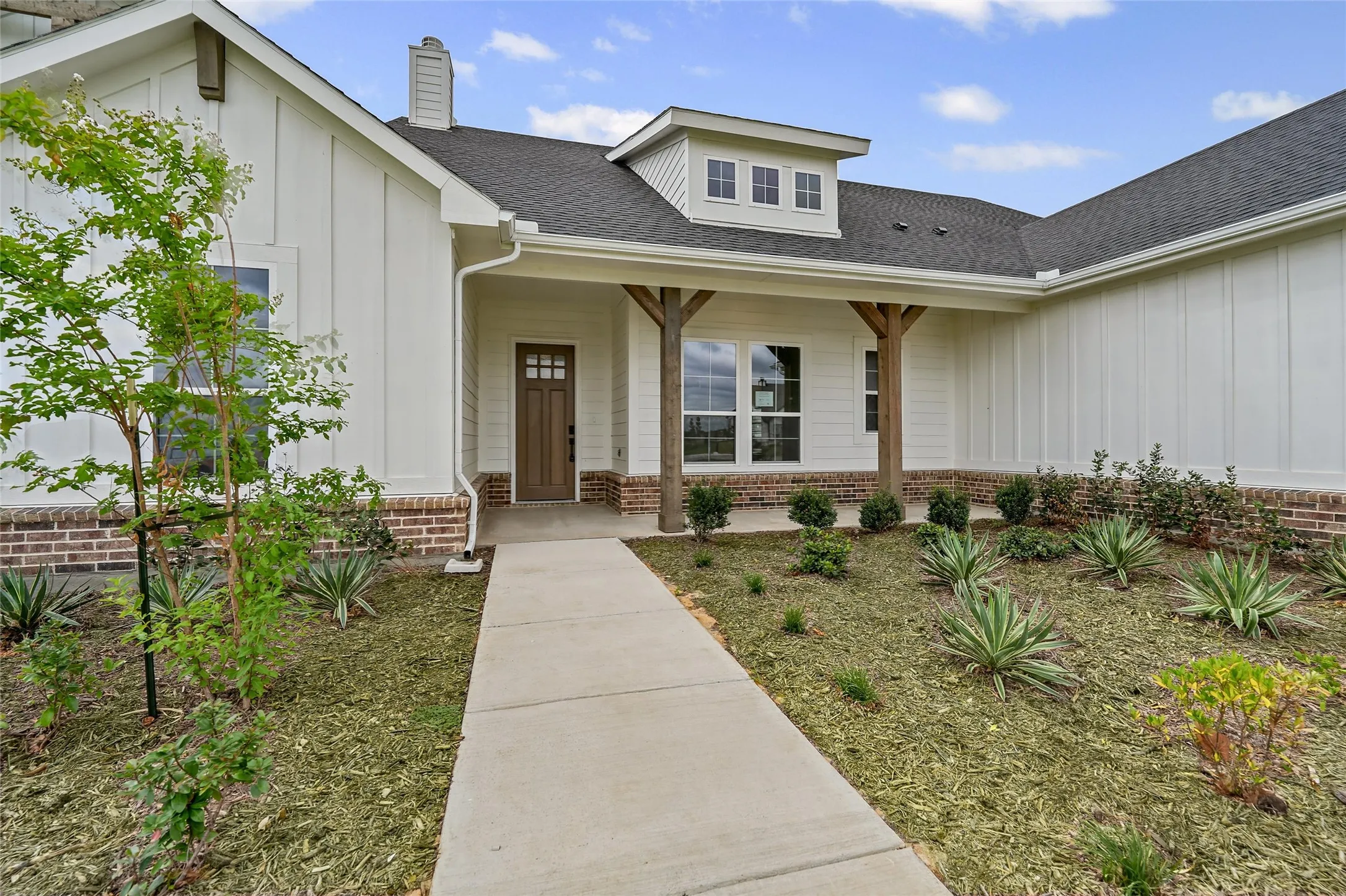 Inviting facade featuring a covered entry, board and batten siding, brick wainscoting, a dark wood-finish front door, and a dormer window