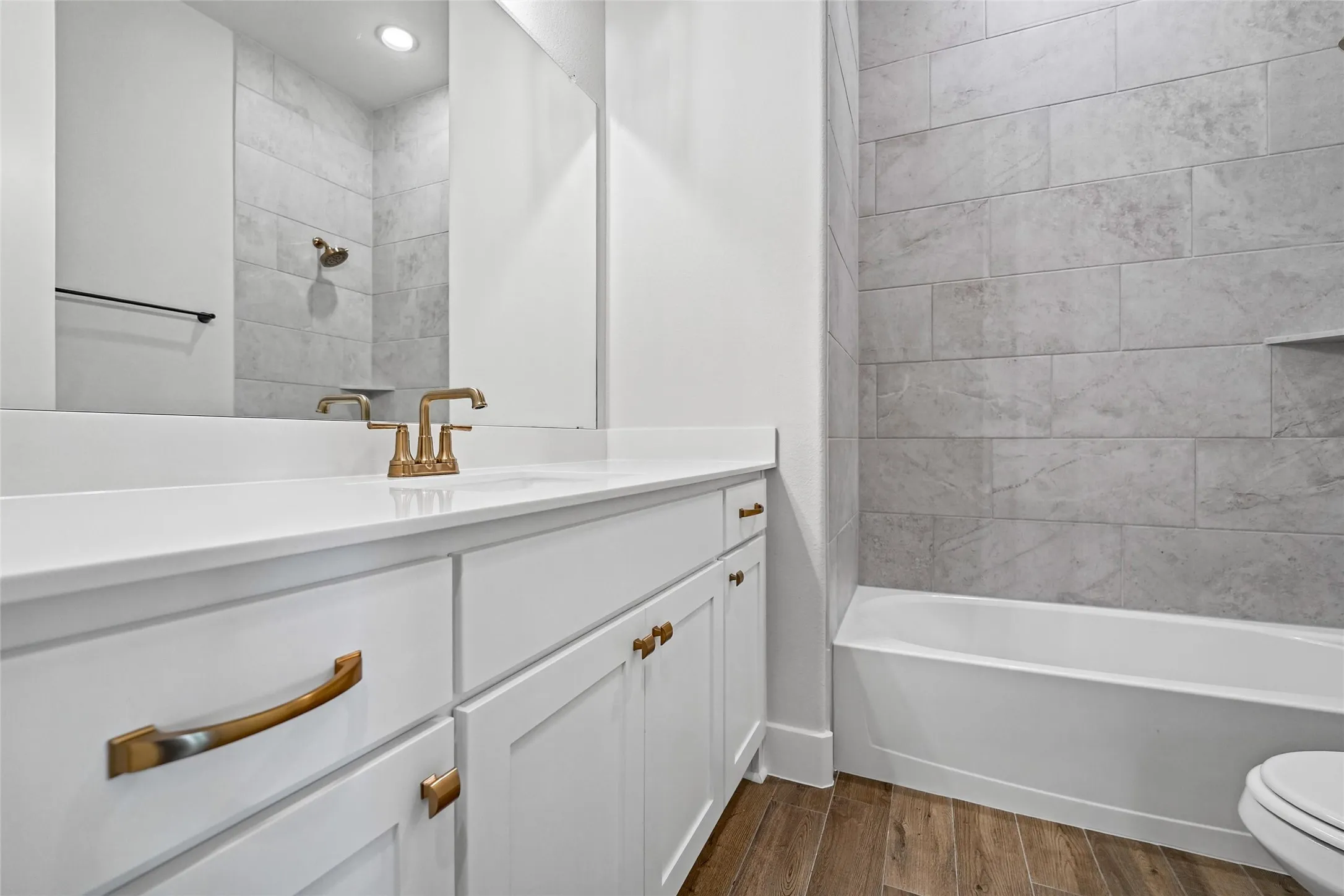 White vanity with gold-tone hardware, white countertop, and wood-finish flooring