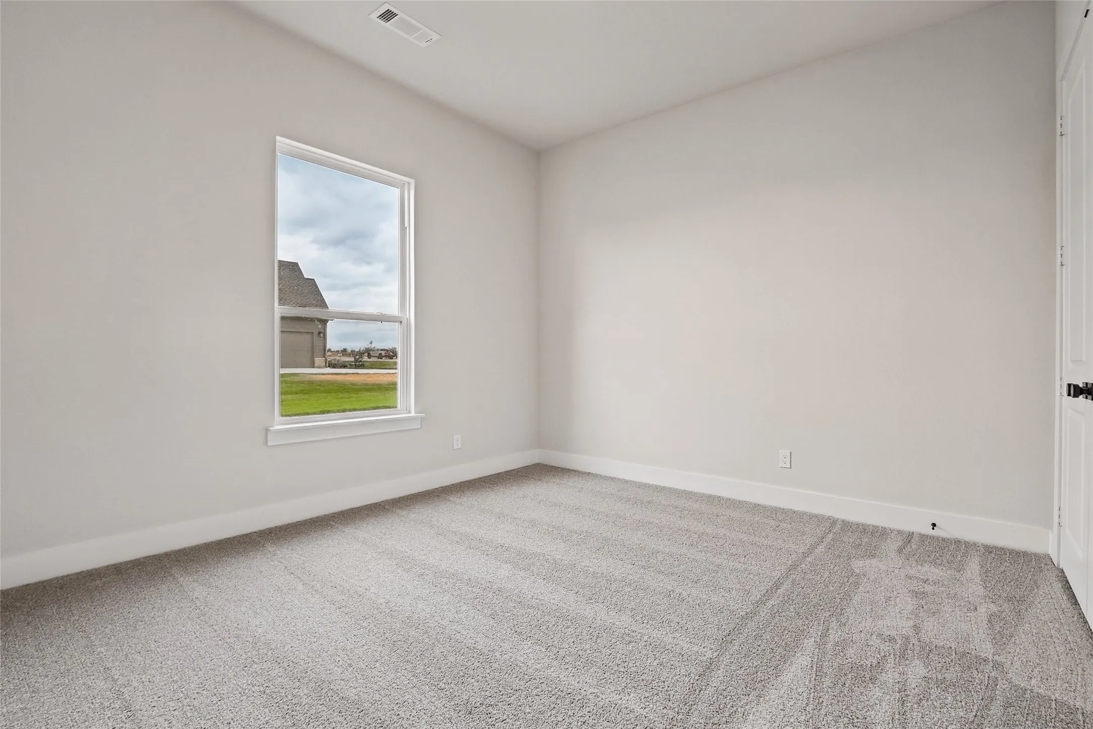 Single-hung window, light-colored walls, light-colored carpeting, white trim, and a white interior door with black hardware