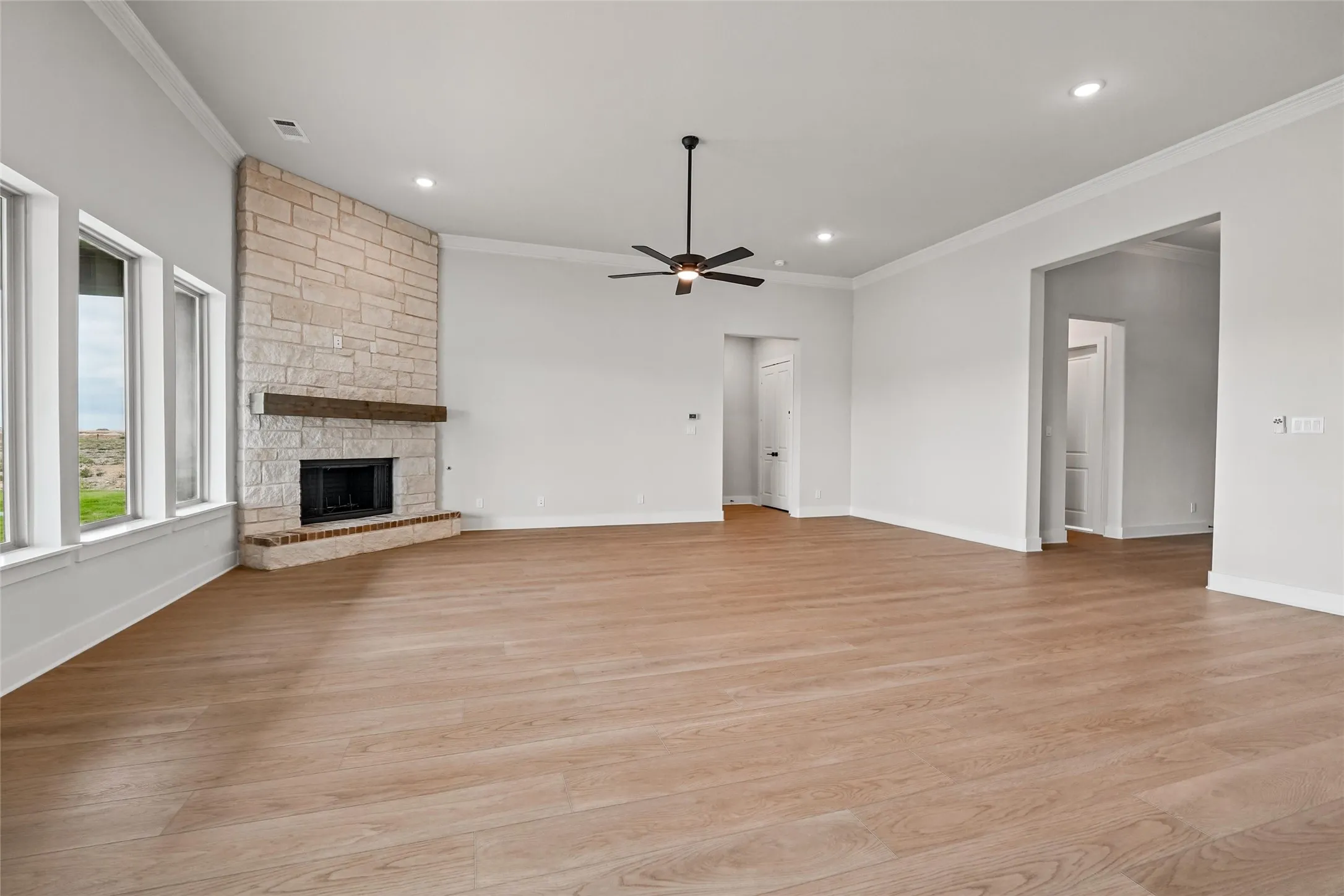 Spacious common area featuring wood-finish flooring, a stone-faced fireplace with a wood mantel, multiple windows, and recessed lighting