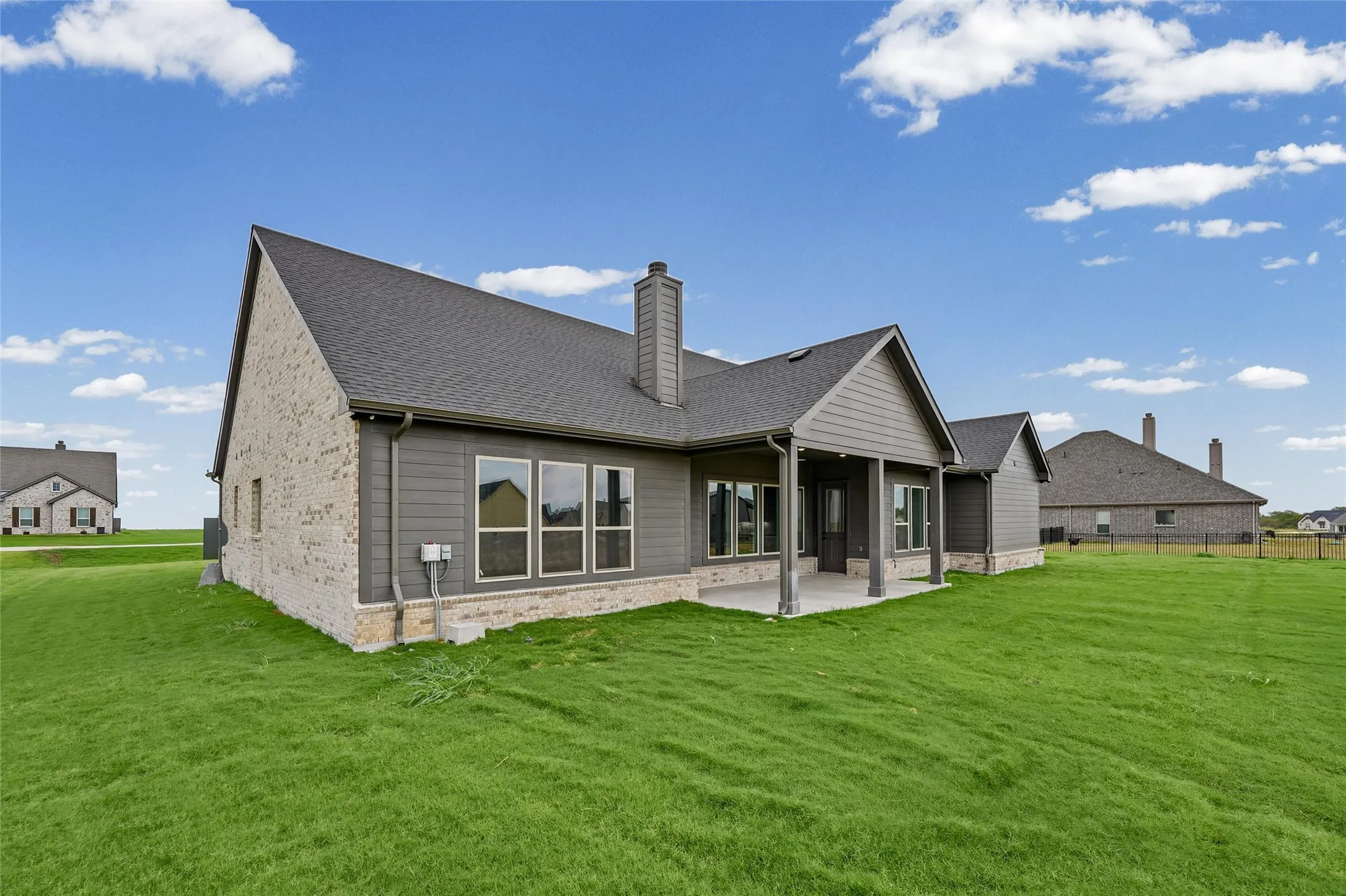 Expansive green lawn, covered patio, brick and siding exterior, multiple windows, and a prominent chimney