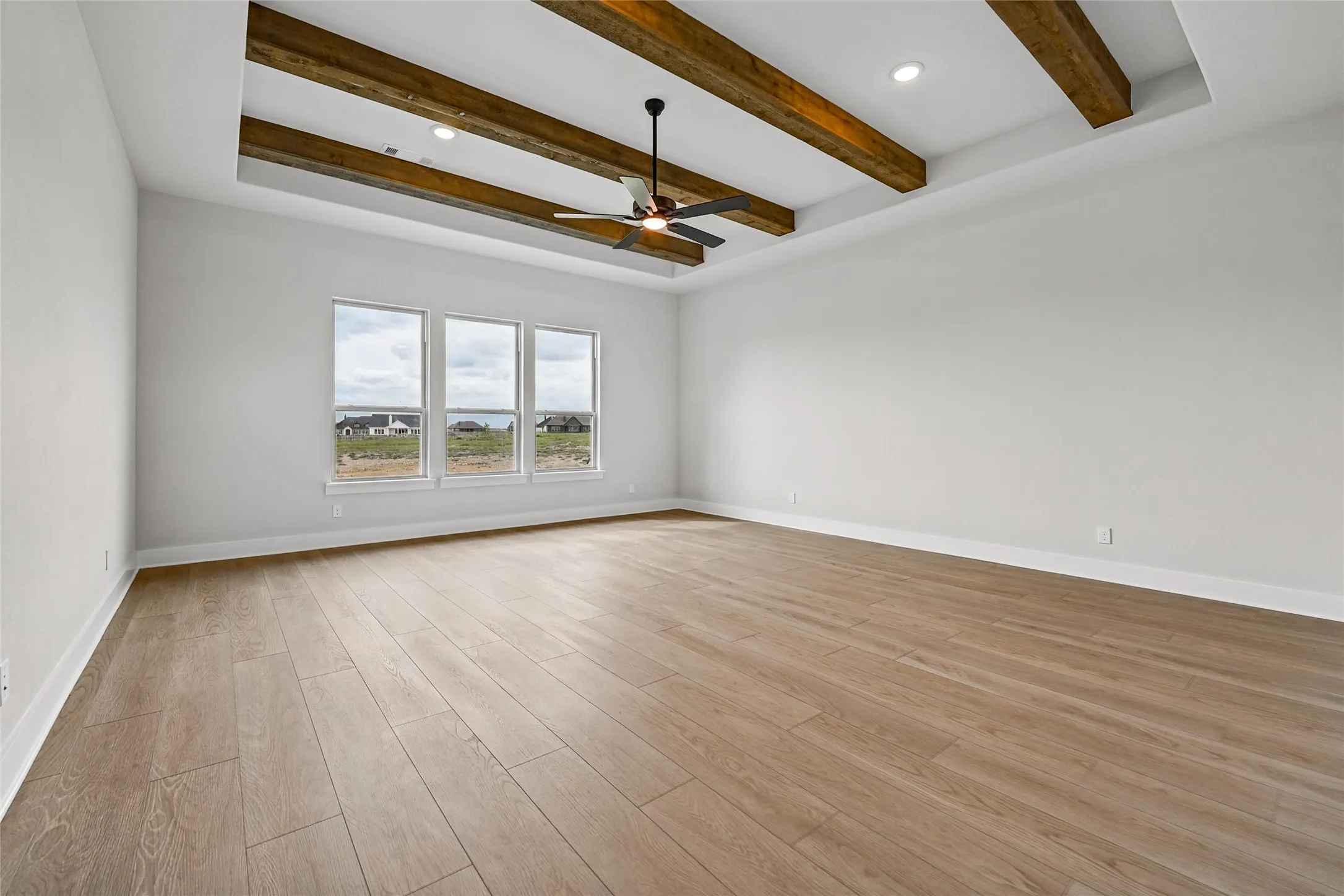 Spacious room featuring a tray ceiling with wood beams, recessed lighting, and a ceiling fan