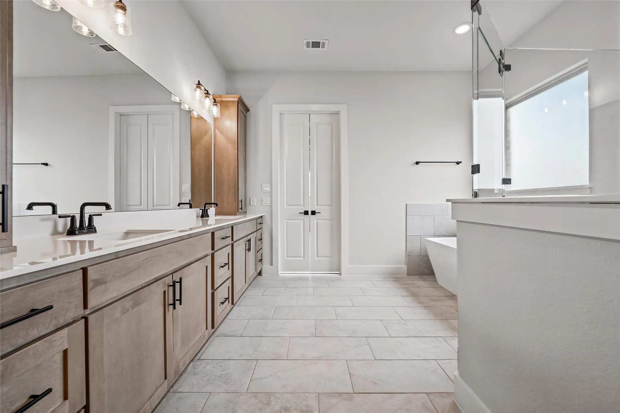 Dual sink vanity with light wood-finish cabinetry and matte black fixtures