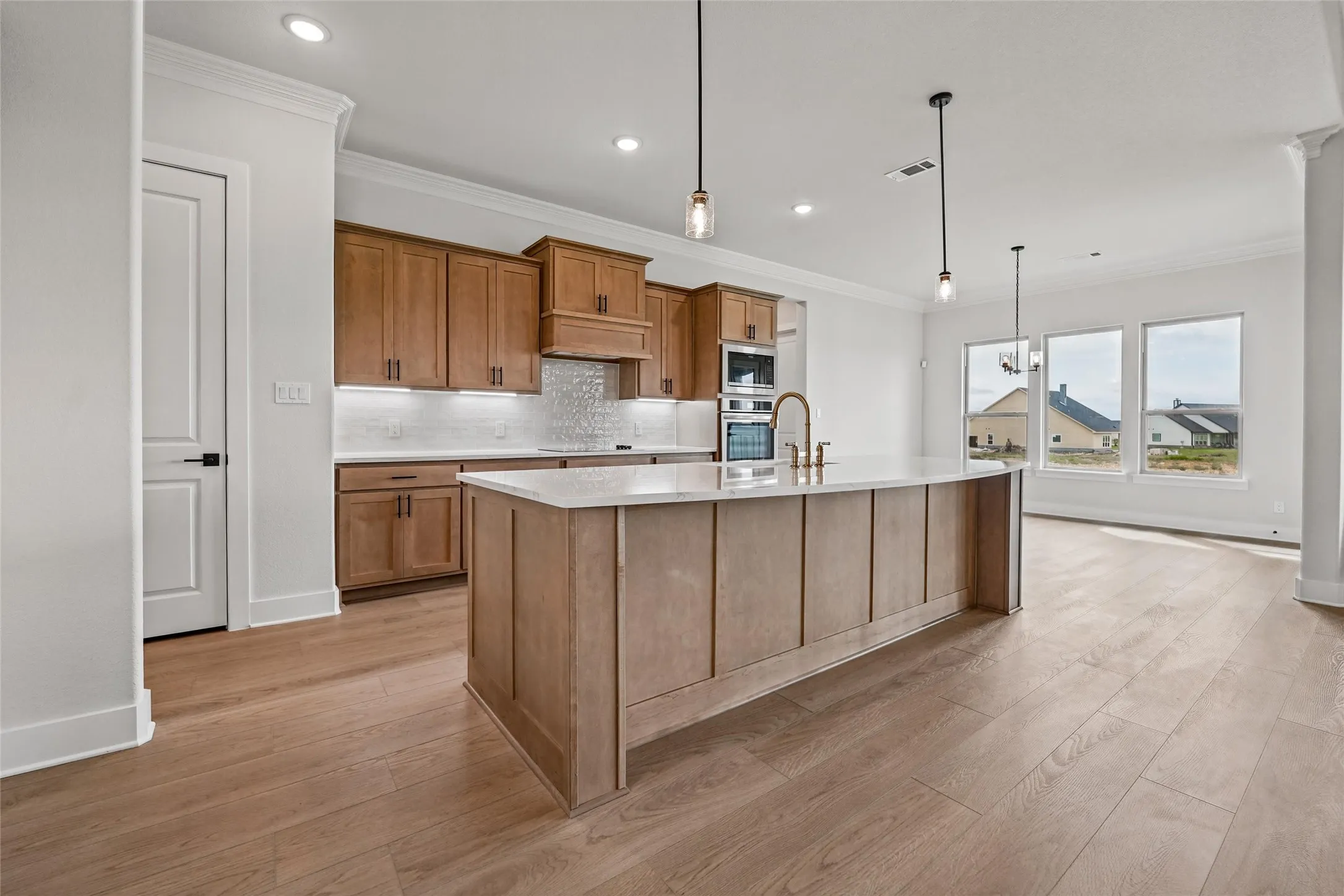 Spacious kitchen featuring a large central island with seating, stainless steel appliances, wood-finish cabinetry, and recessed lighting