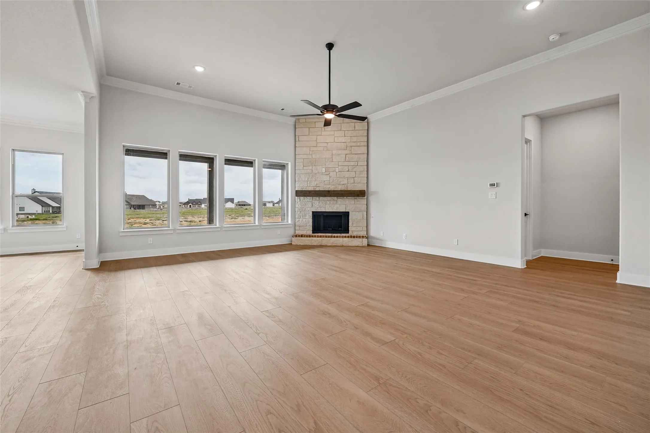 Spacious living area featuring wood-finish flooring, a stone fireplace with a wood mantel, and multiple windows