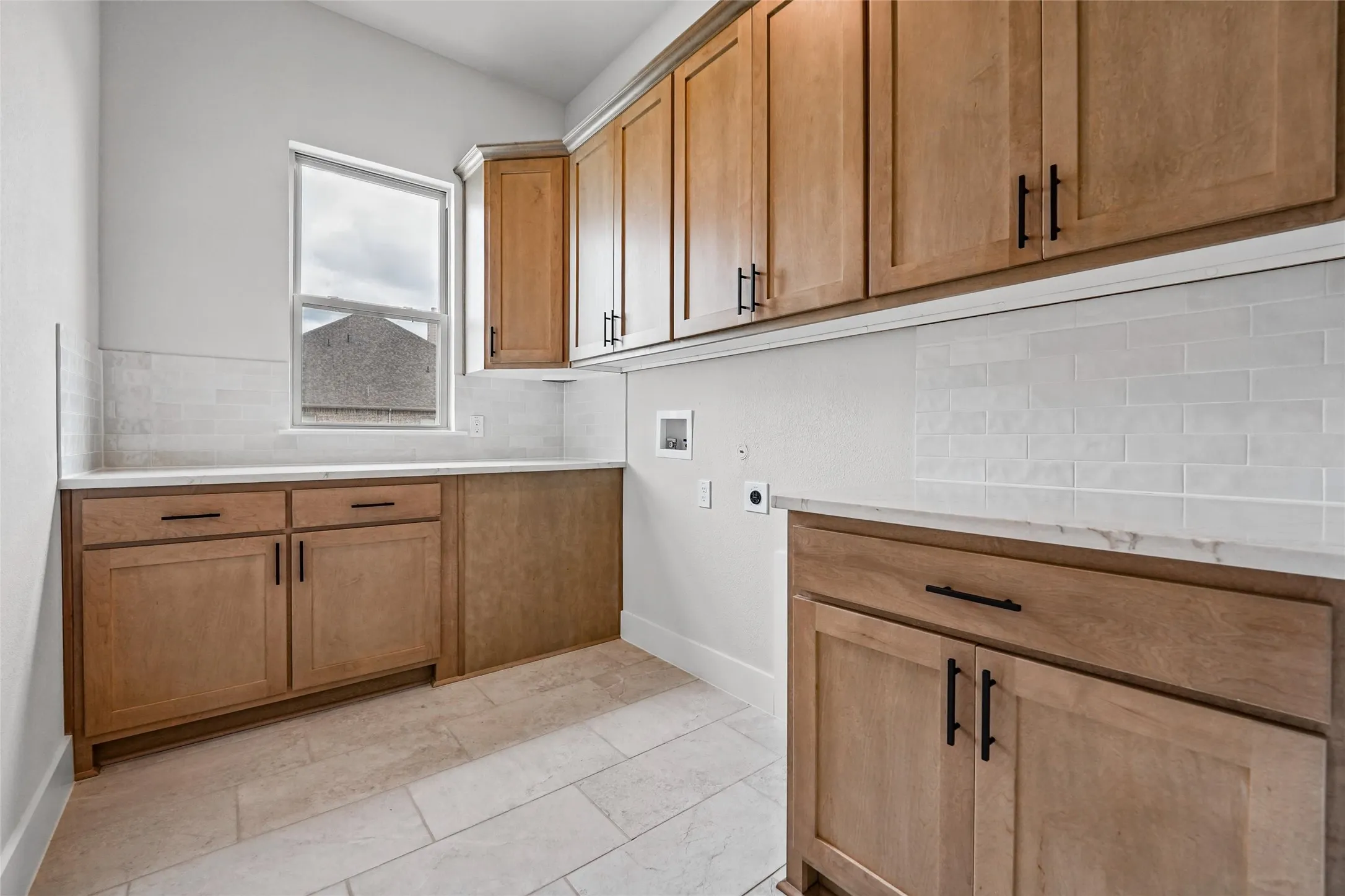 Spacious utility area featuring light wood-finish cabinetry, solid surface countertops, light subway tile backsplash, and tile flooring