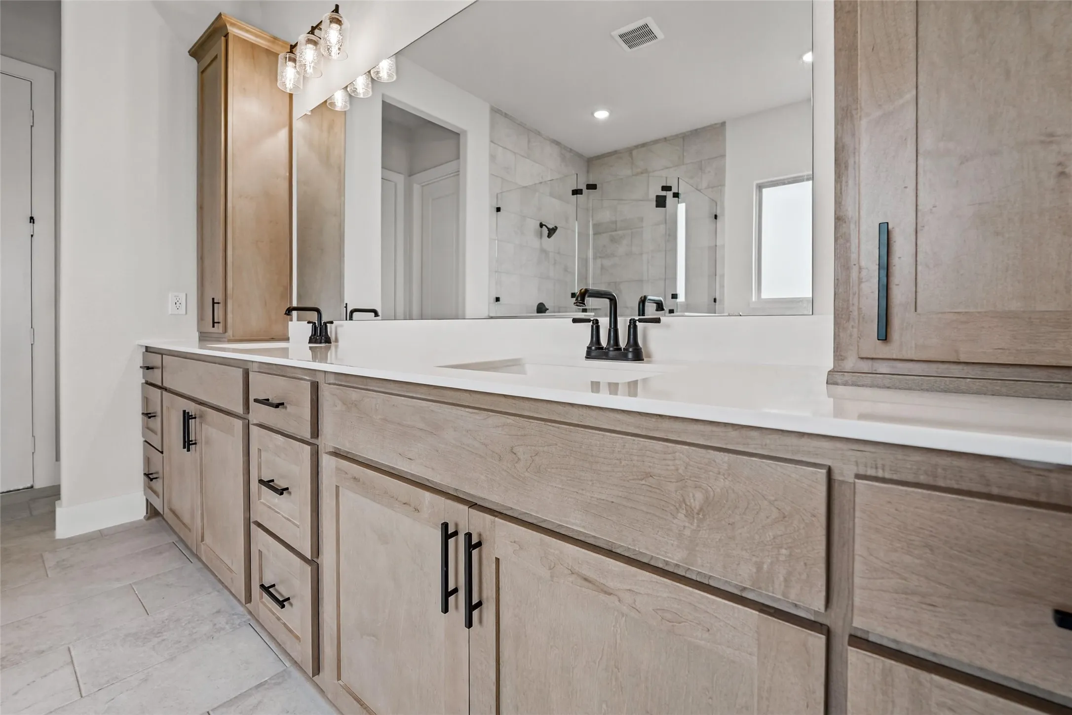 Dual vanity with light wood-finish cabinetry, white countertop, and matte black fixtures