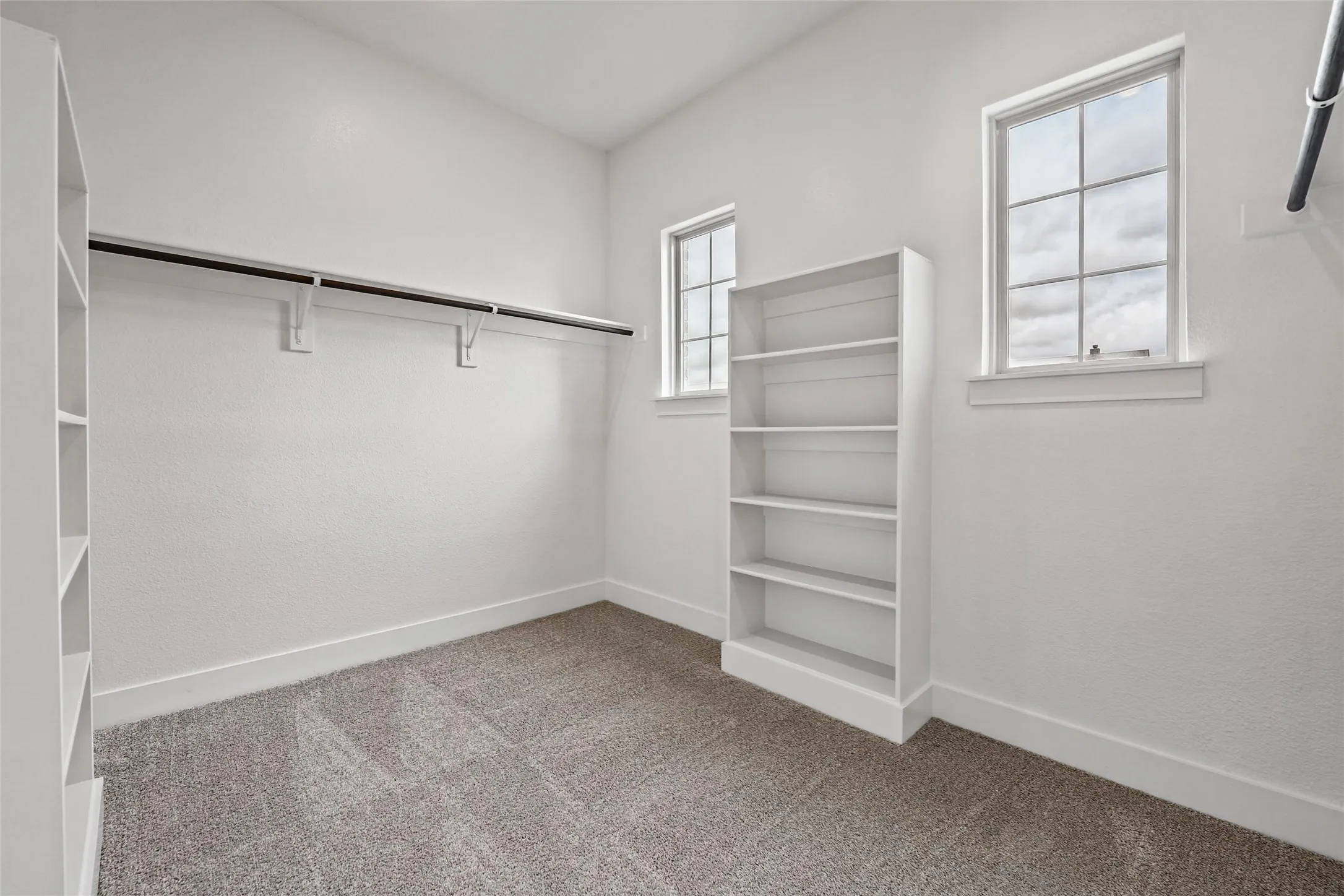 Built-in shelving, two windows, carpet flooring, and a clothing rod with shelving