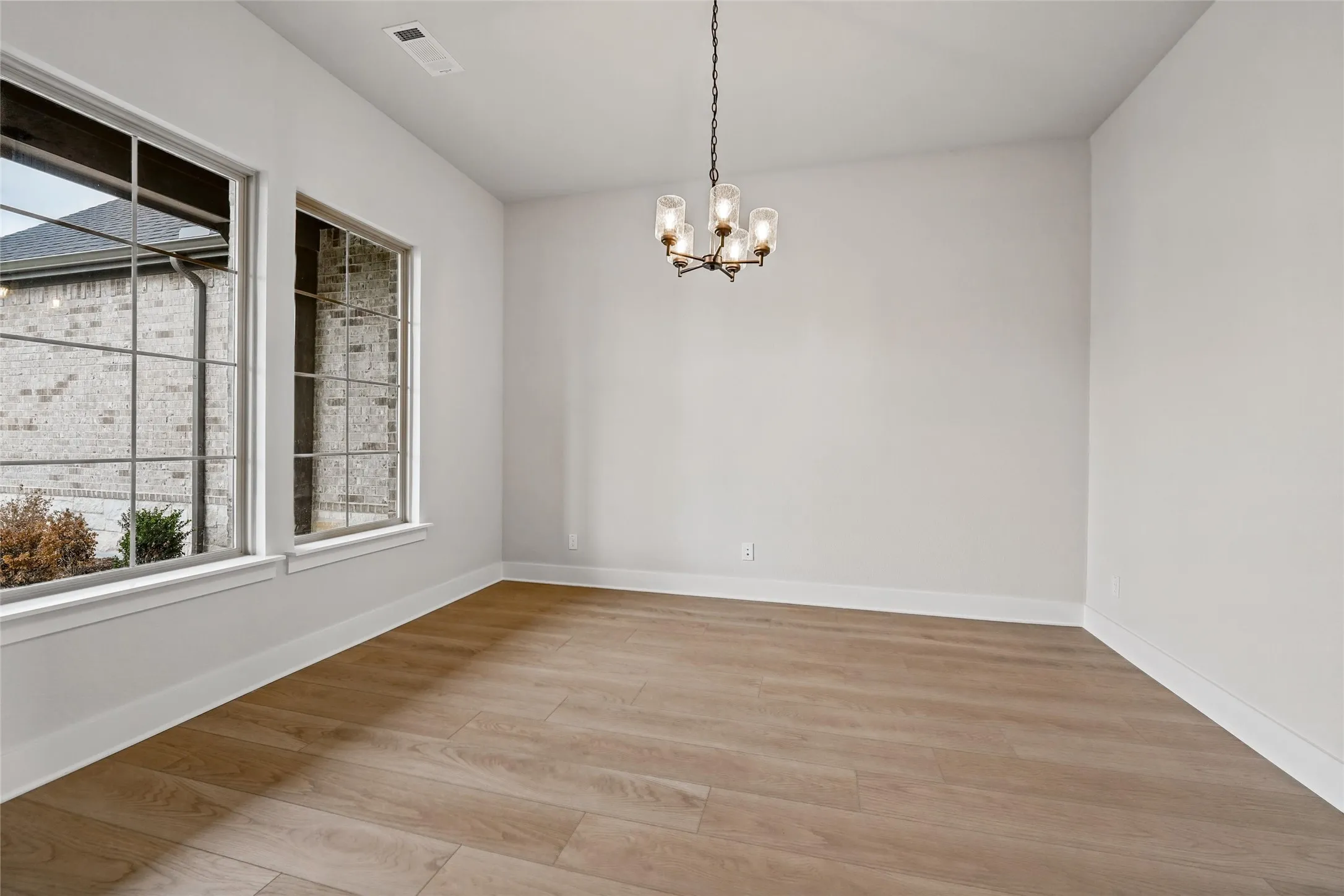 Spacious room featuring wood-finish flooring, two large multi-pane windows, a bronze-finish chandelier, and light-toned wall finishes