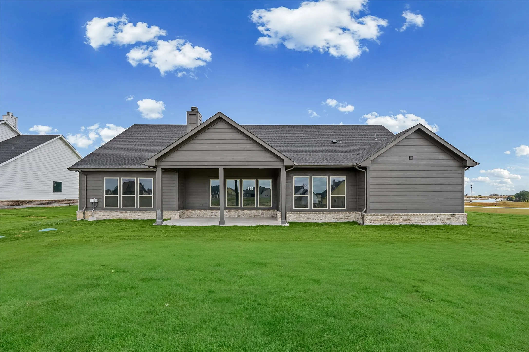 Expansive green lawn, covered patio, multiple large windows, and a shingle roof