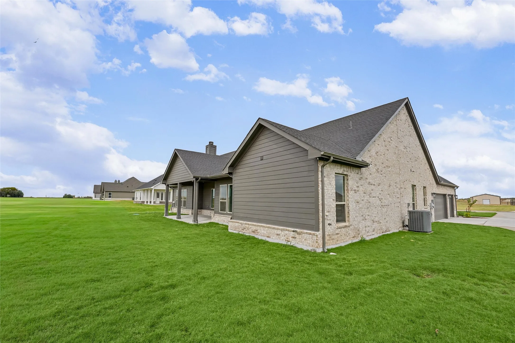 Brick and siding exterior with a covered patio, multiple windows, and a two-car garage