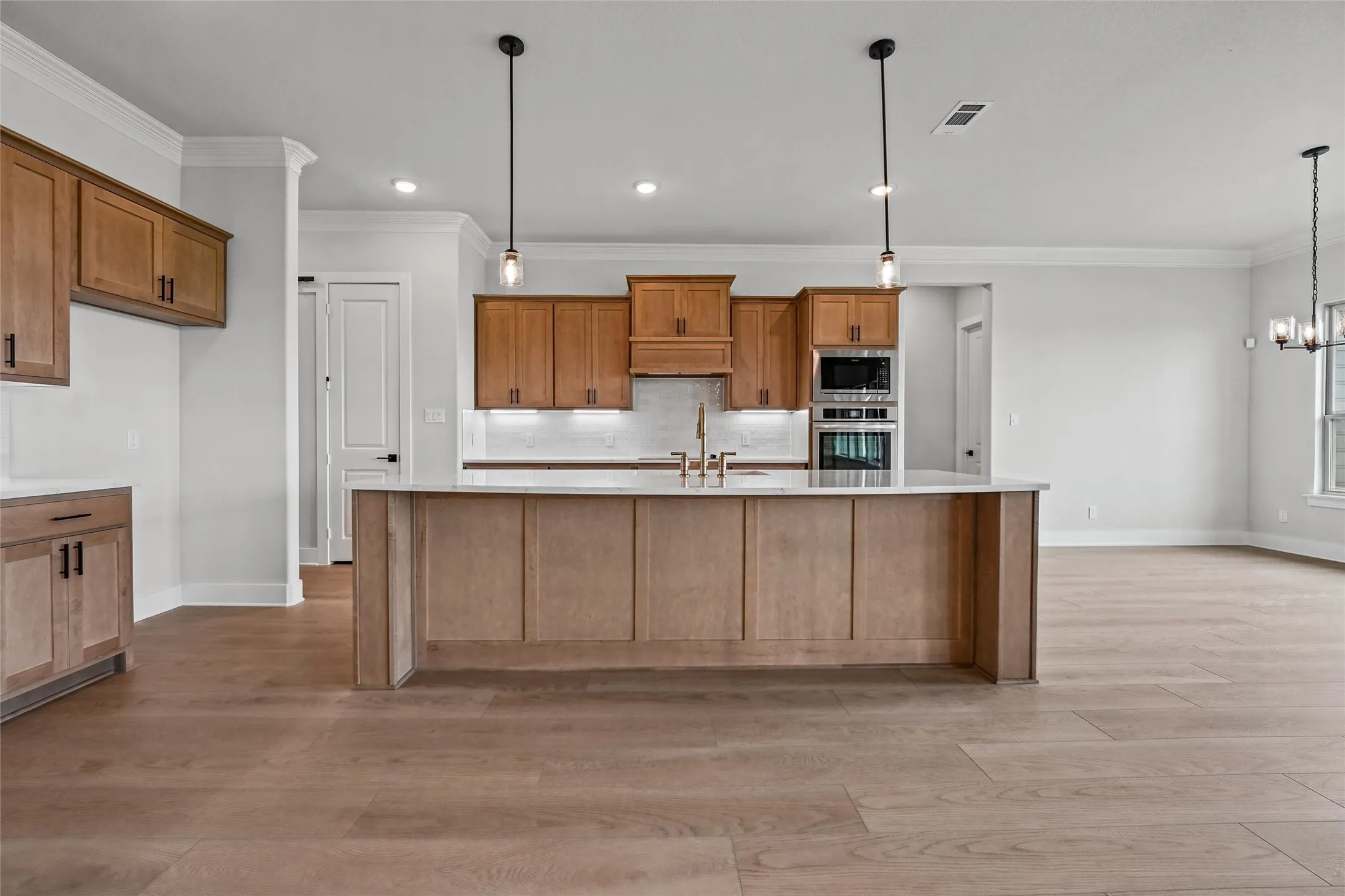 Kitchen featuring wood-finish cabinetry, built-in stainless steel appliances, a center island with countertop, and pendant lighting