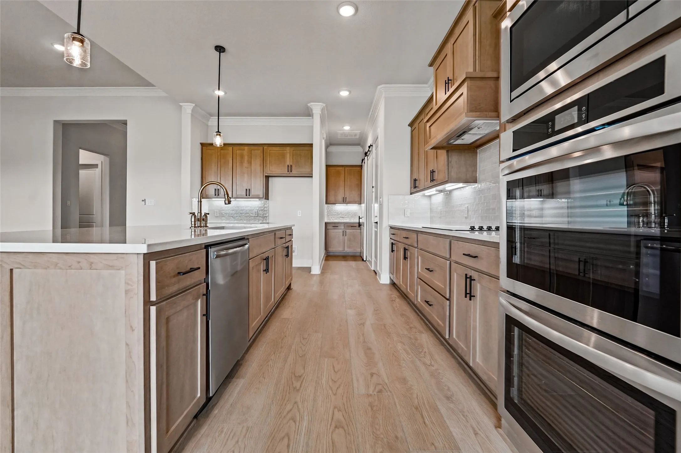 Kitchen featuring wood-finish flooring, stainless steel appliances, an island with an undermount sink, pendant lighting, and a tile backsplash