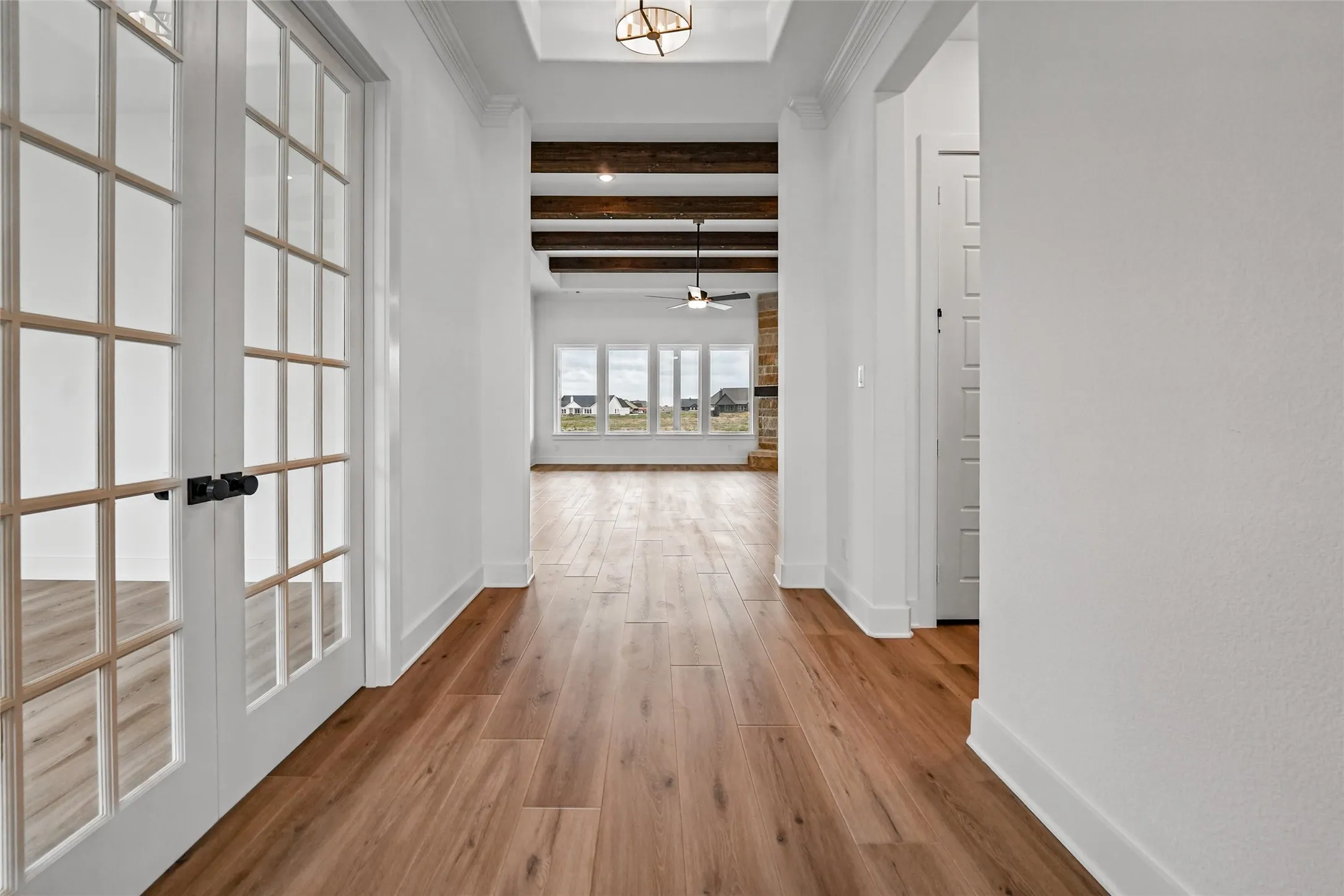 Hallway with wood-finish flooring, white walls, exposed ceiling beams, and French doors