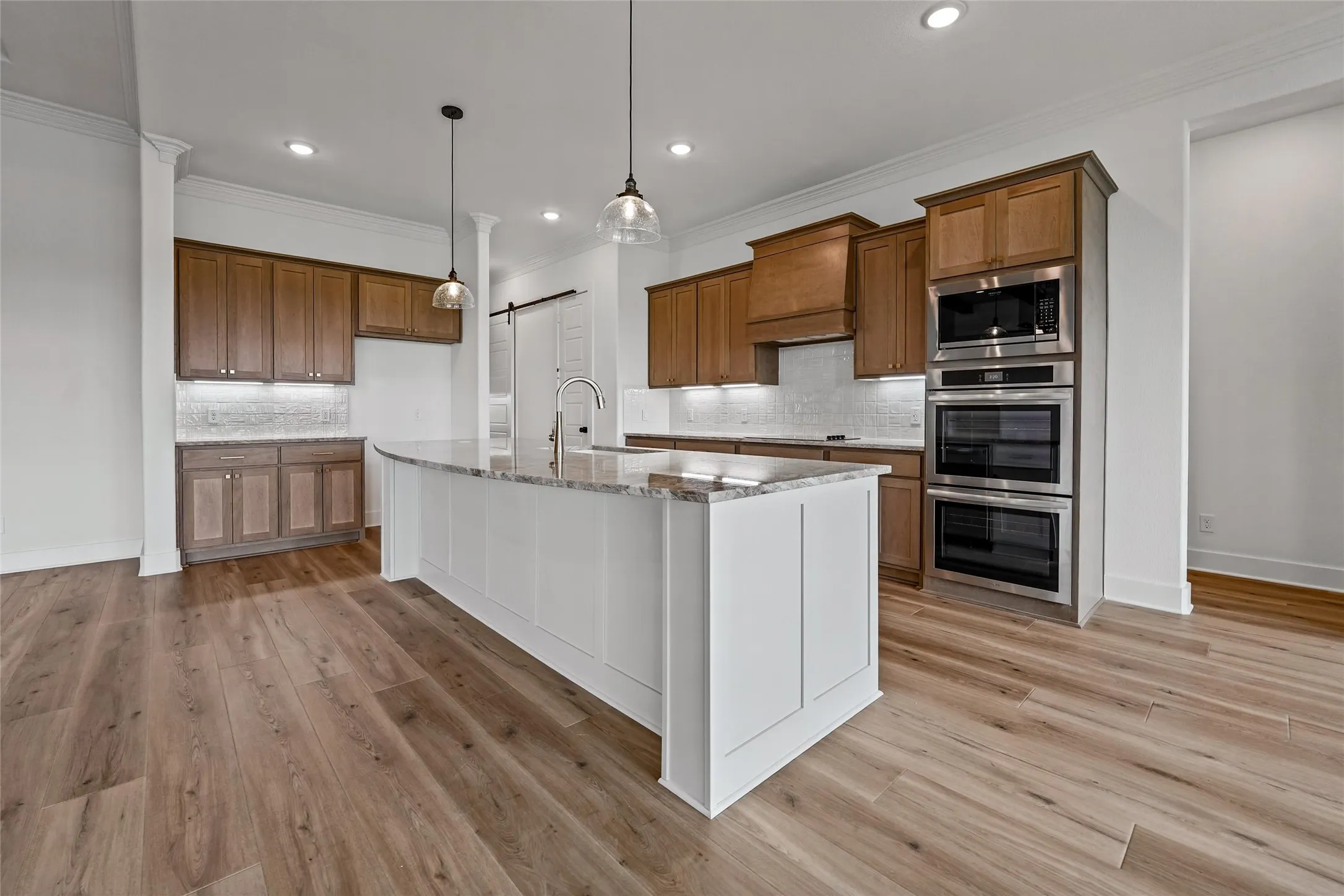 Spacious kitchen featuring a large central island, wood-finish flooring, recessed lighting, and stainless steel built-in double ovens
