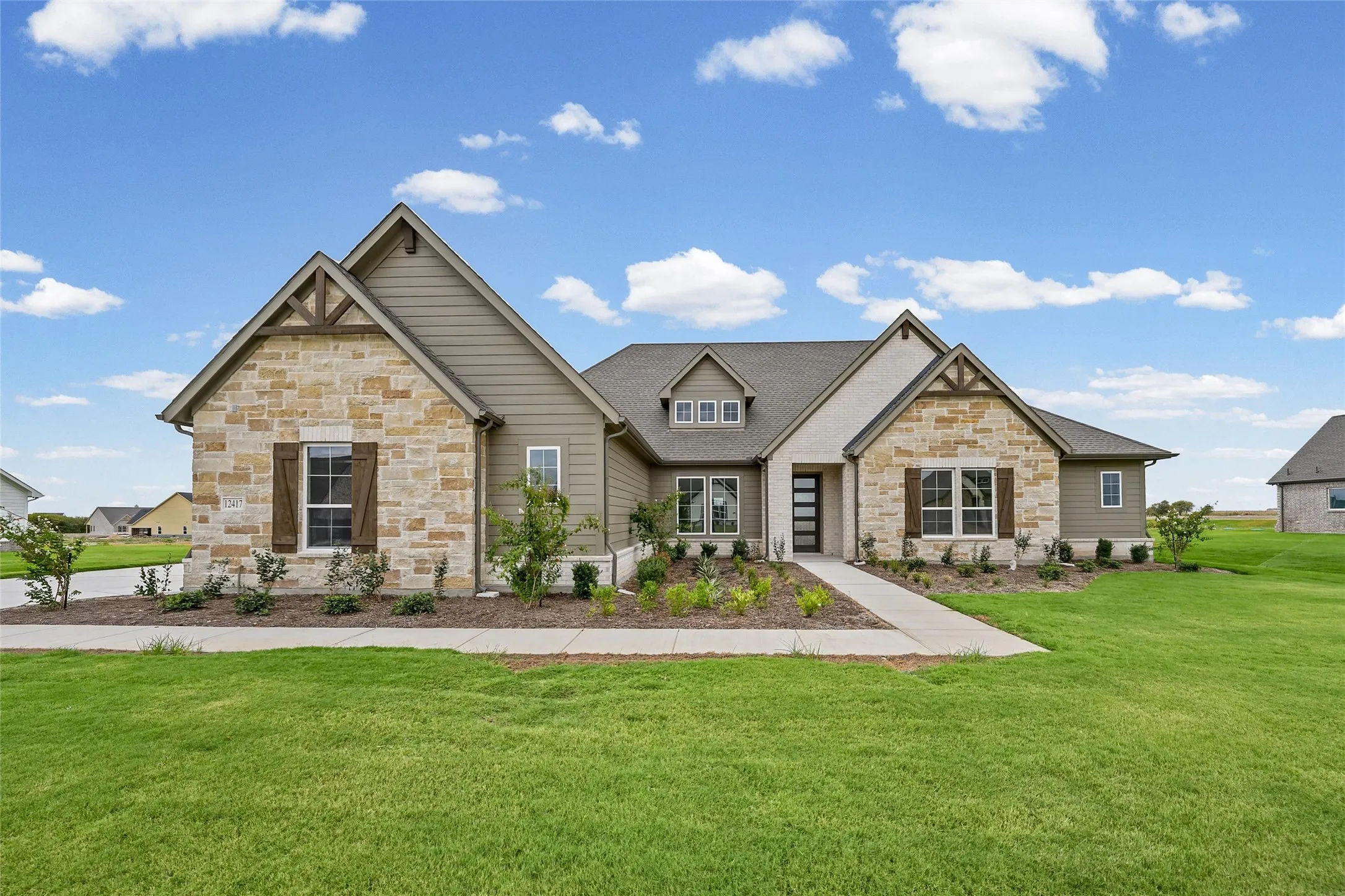 Exterior featuring stone and siding finishes, gabled rooflines, decorative wooden shutters, a paved walkway, and manicured landscaping