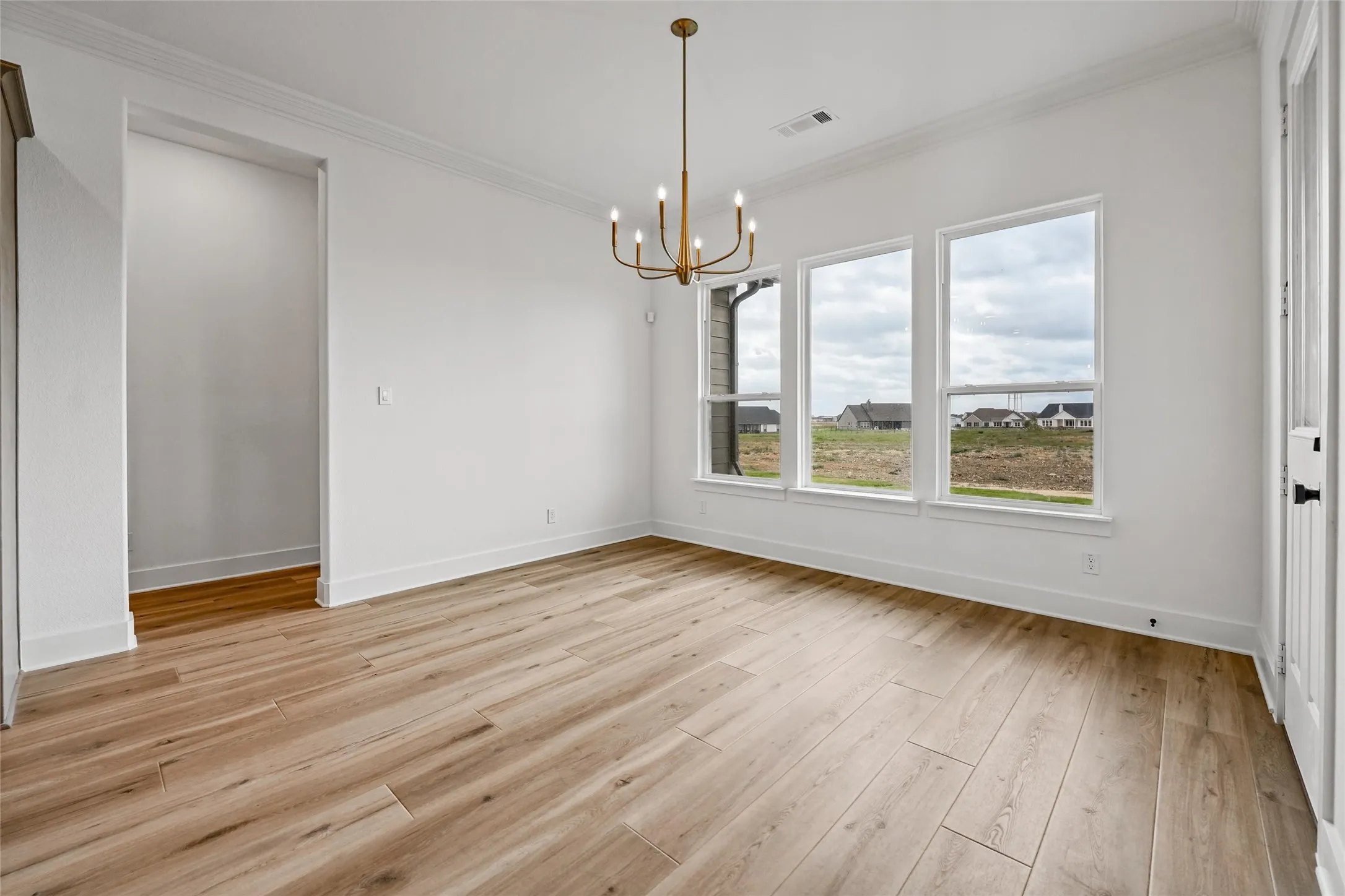 Spacious room featuring wood-finish flooring, ample natural light from multiple windows, a contemporary chandelier, and crisp white walls