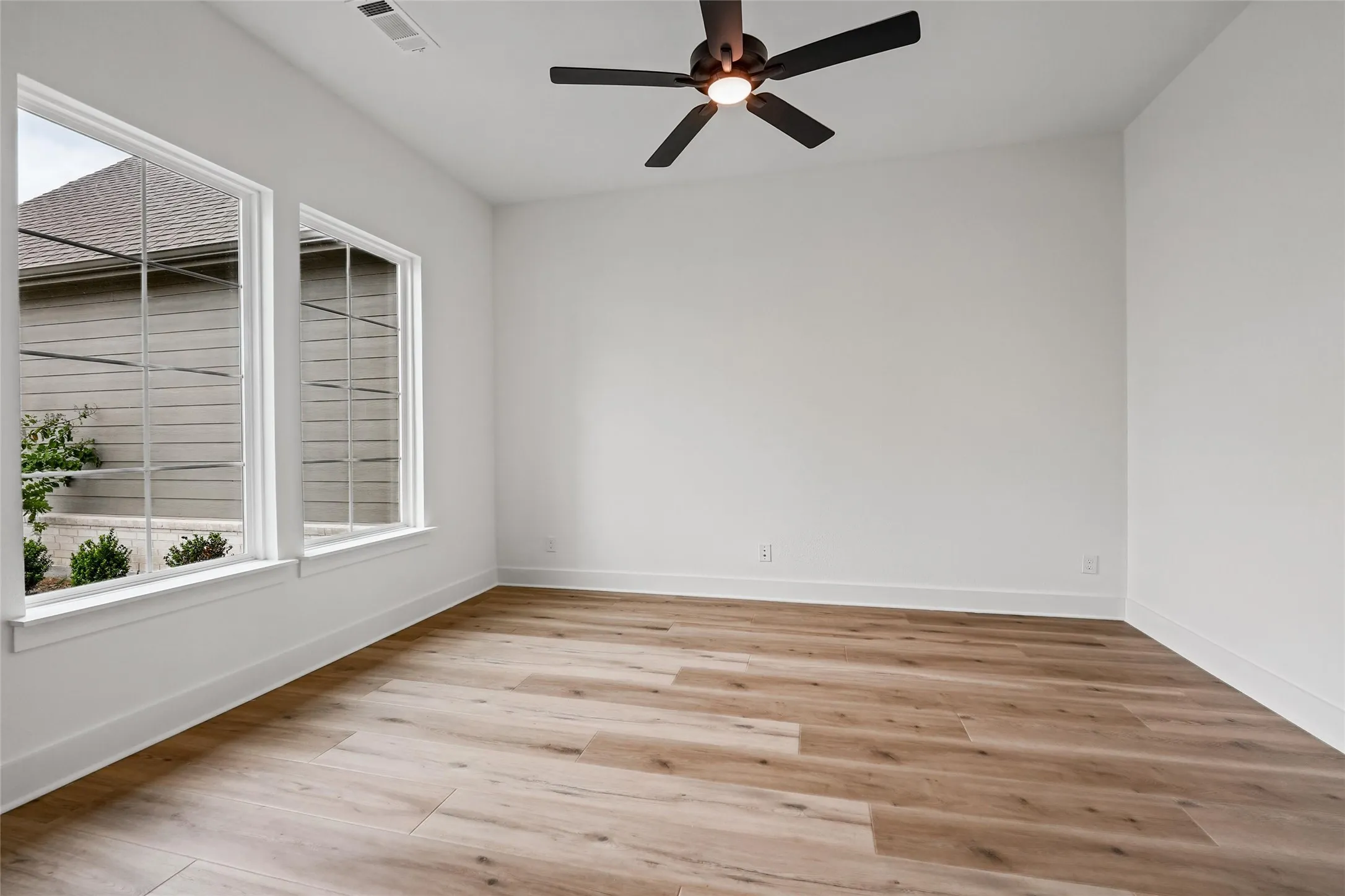 Two expansive windows, wood-finish flooring, and a ceiling fan with integrated lighting