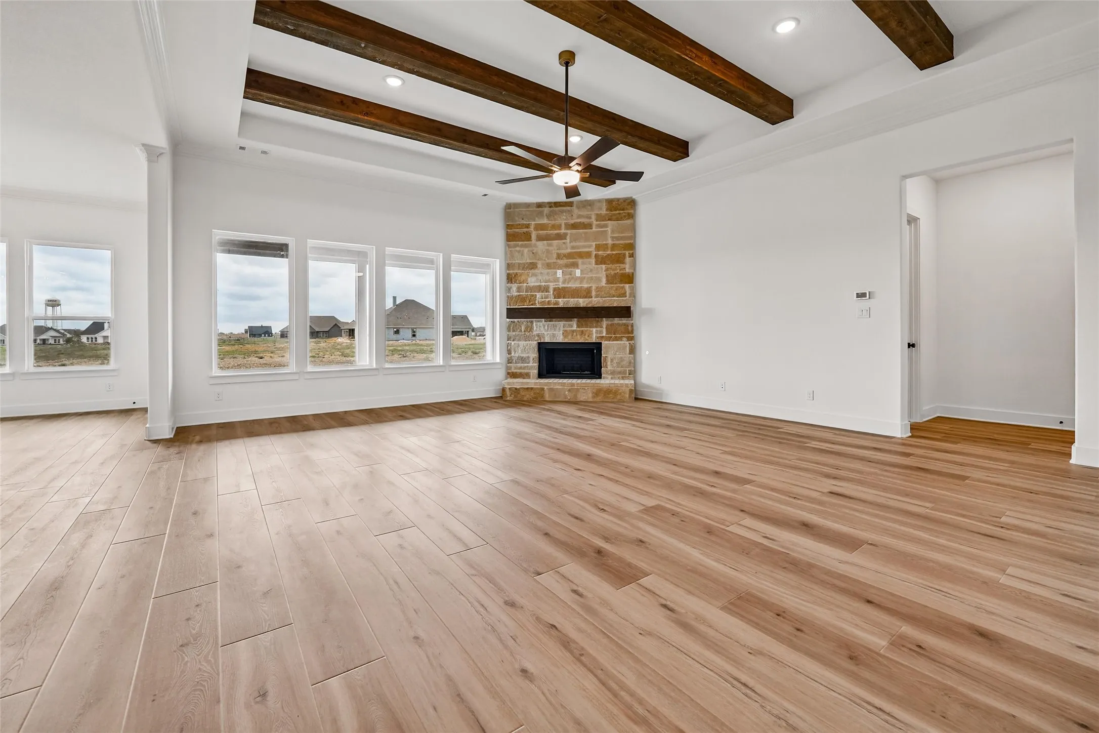 Spacious living area featuring wood-finish flooring, a stone-clad fireplace, and an exposed beam ceiling
