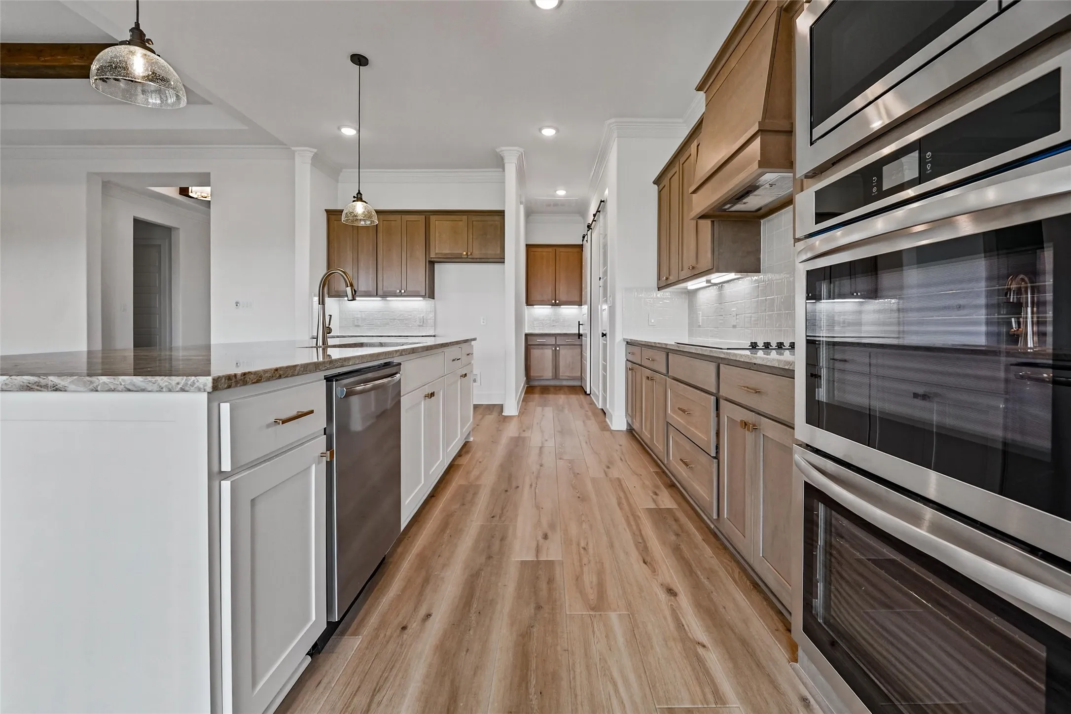 Gourmet kitchen featuring wood-finish flooring, two-tone cabinetry, stainless steel appliances, stone countertops, and a subway tile backsplash