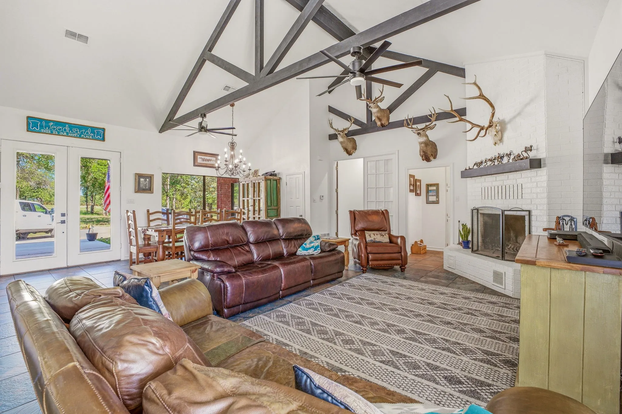 Spacious living area featuring a vaulted ceiling with exposed beams, ceiling fans, and a white brick fireplace
