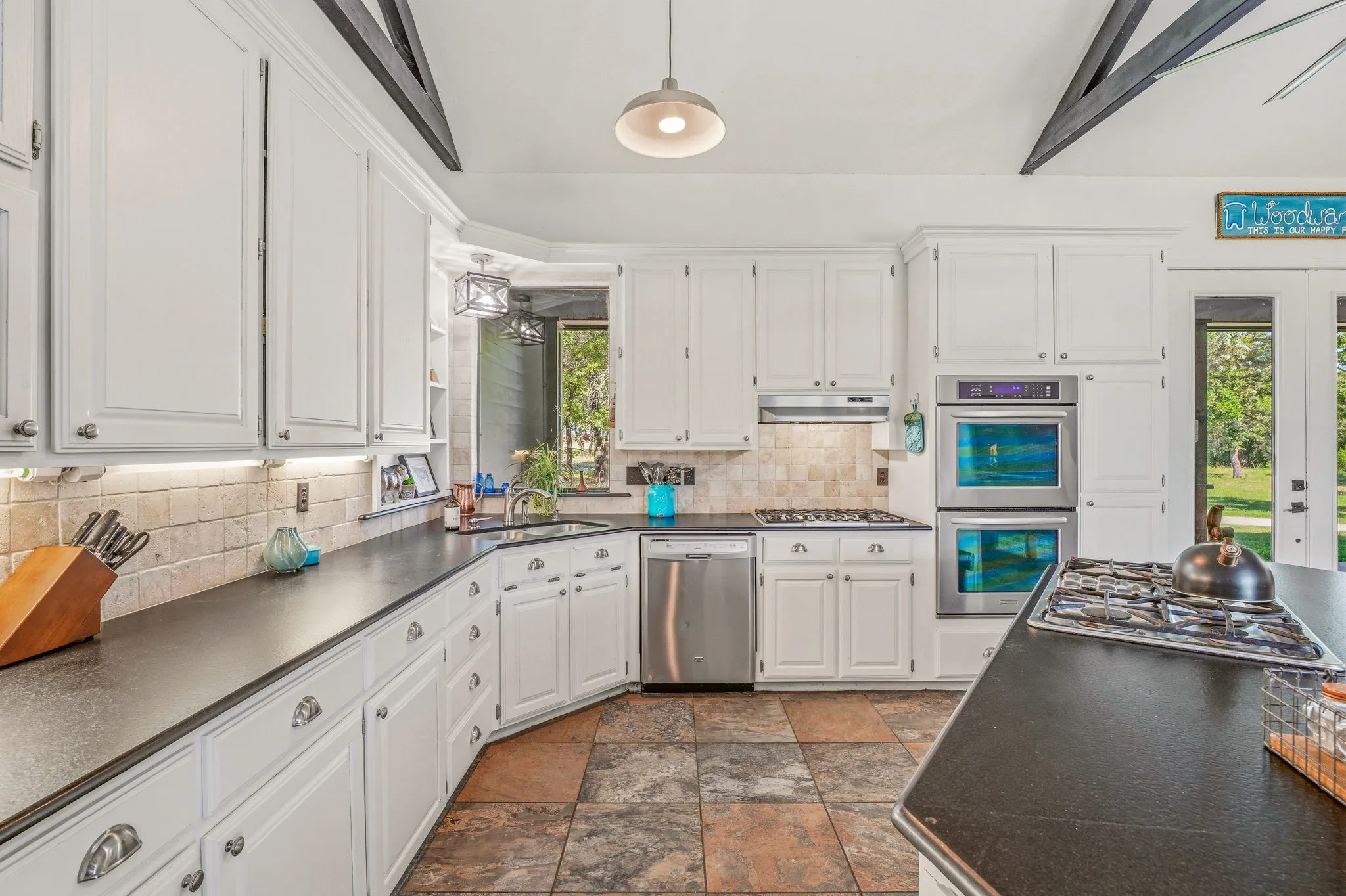 Kitchen featuring white cabinetry, dark countertops, a tile backsplash, stainless steel double ovens, and tile flooring
