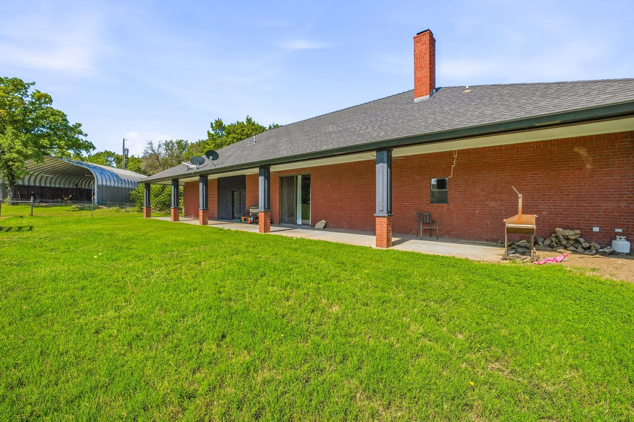 Expansive green lawn with a covered back patio, brick exterior, and a large quonset hut structure
