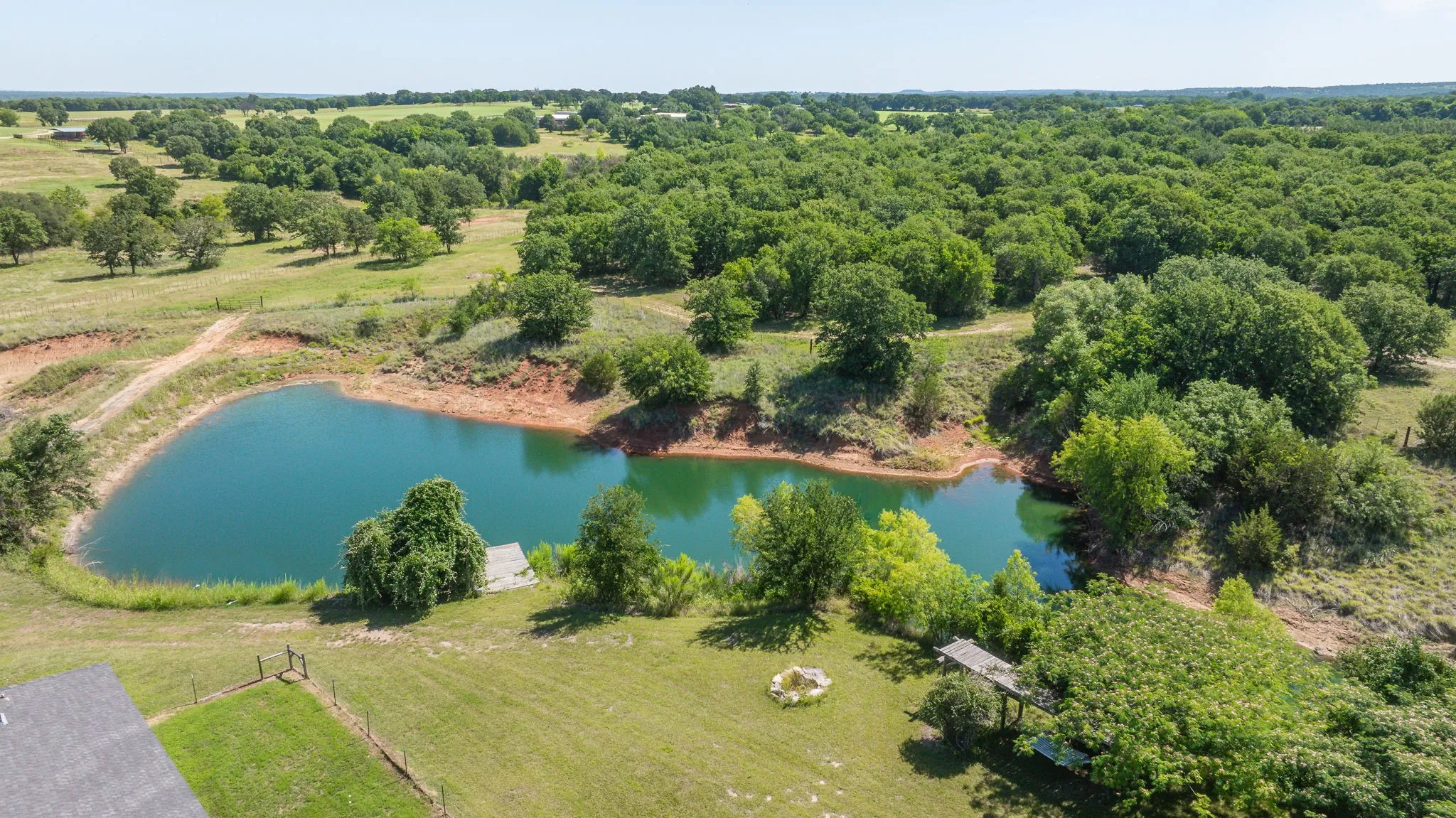 Expansive pond with a wooden dock, surrounded by mature trees and verdant fields